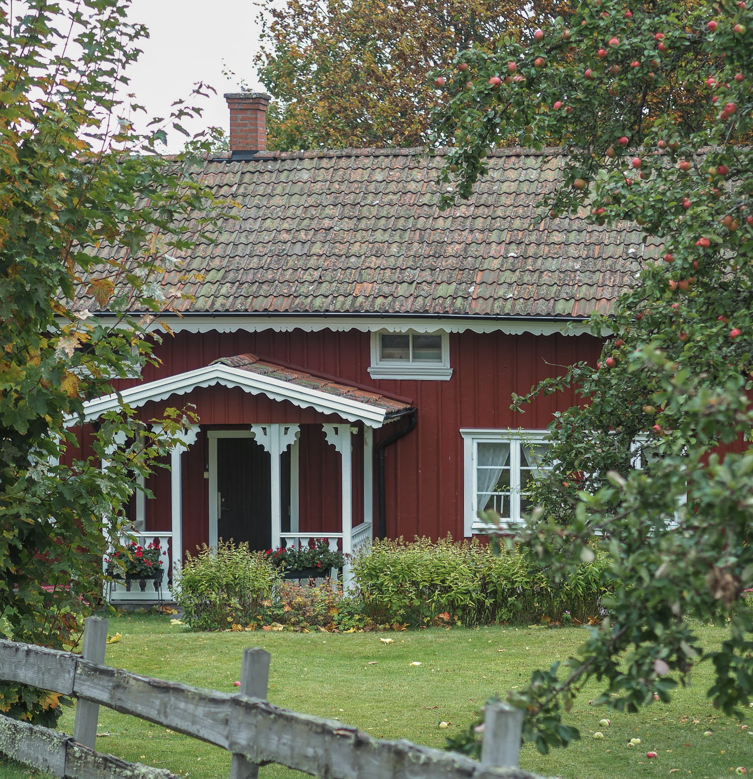 En bild på ett rött torp inbäddat i lummig grönska.