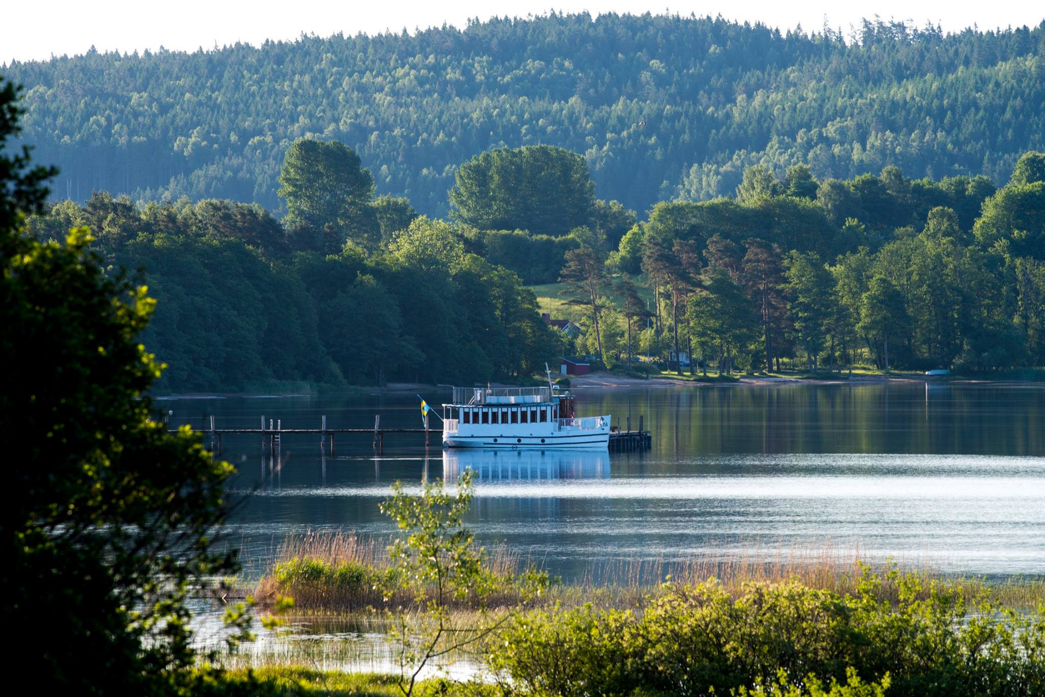 En vit båt flyter på spegelblank vattenyta