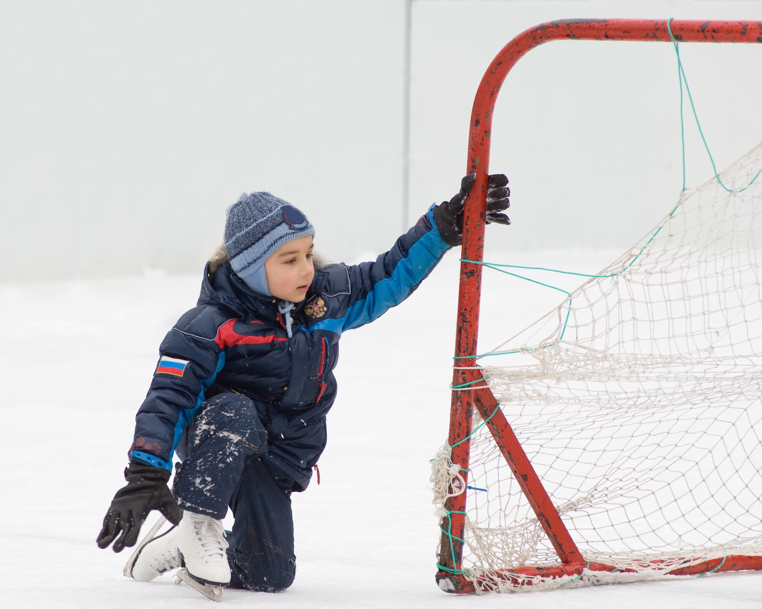 En pojke som sitter ute på is vid ett hockeymål