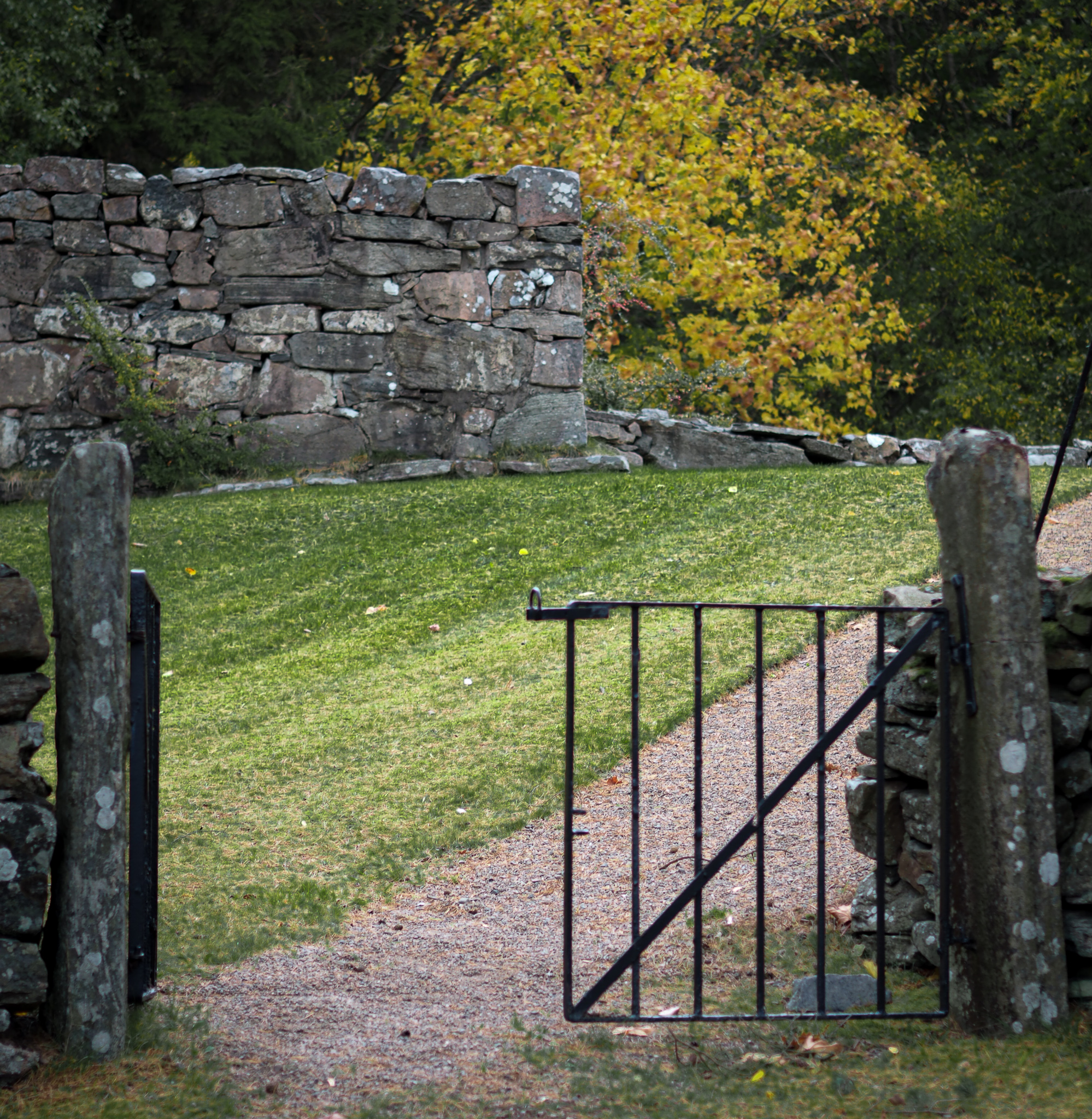 En grind och en grusgång som leder upp till en stenmur som är en del av en kyrkoruin