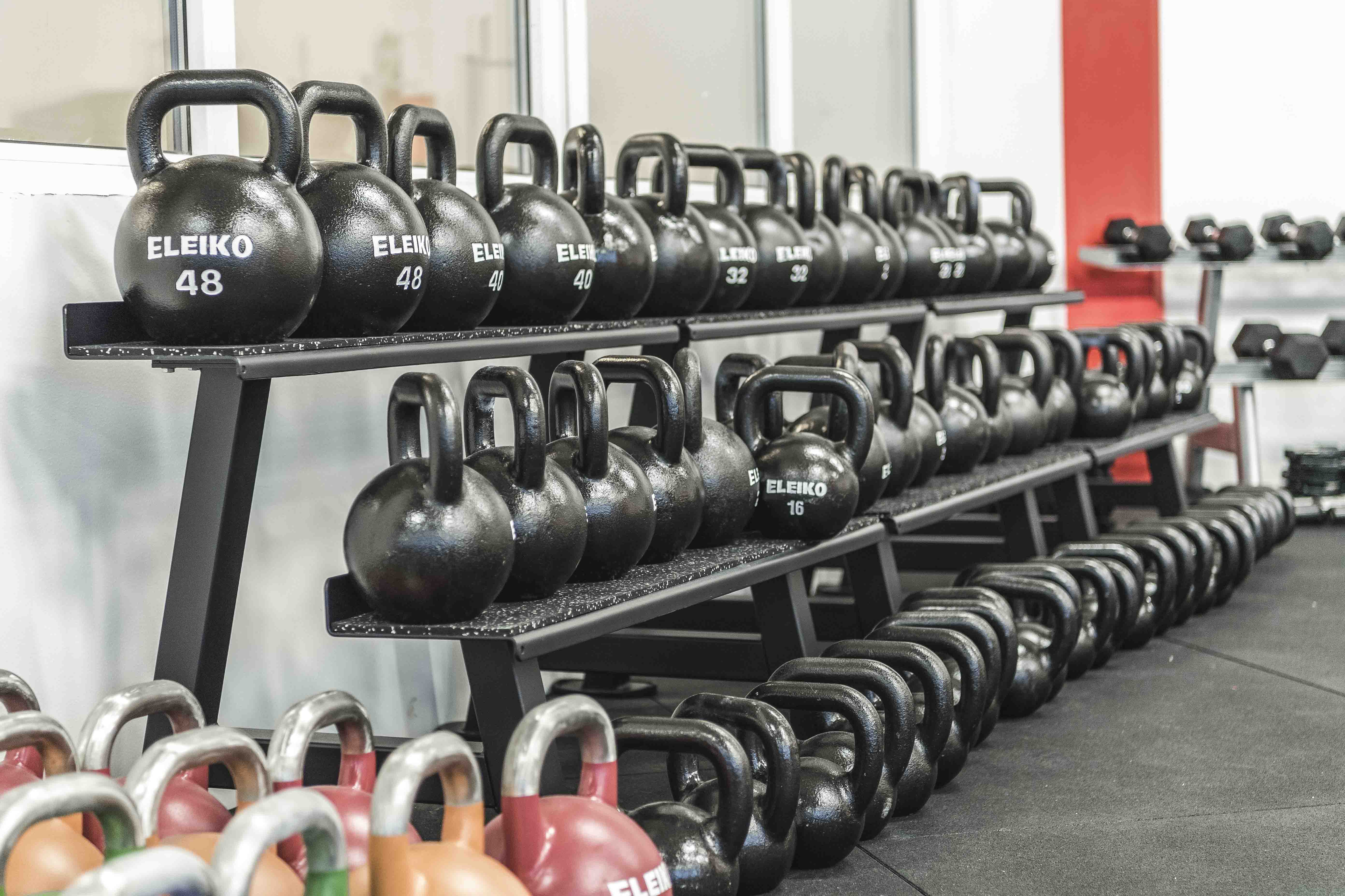 En bild på massa träningsredskap som står uppradade längs en vägg inne på ett gym.