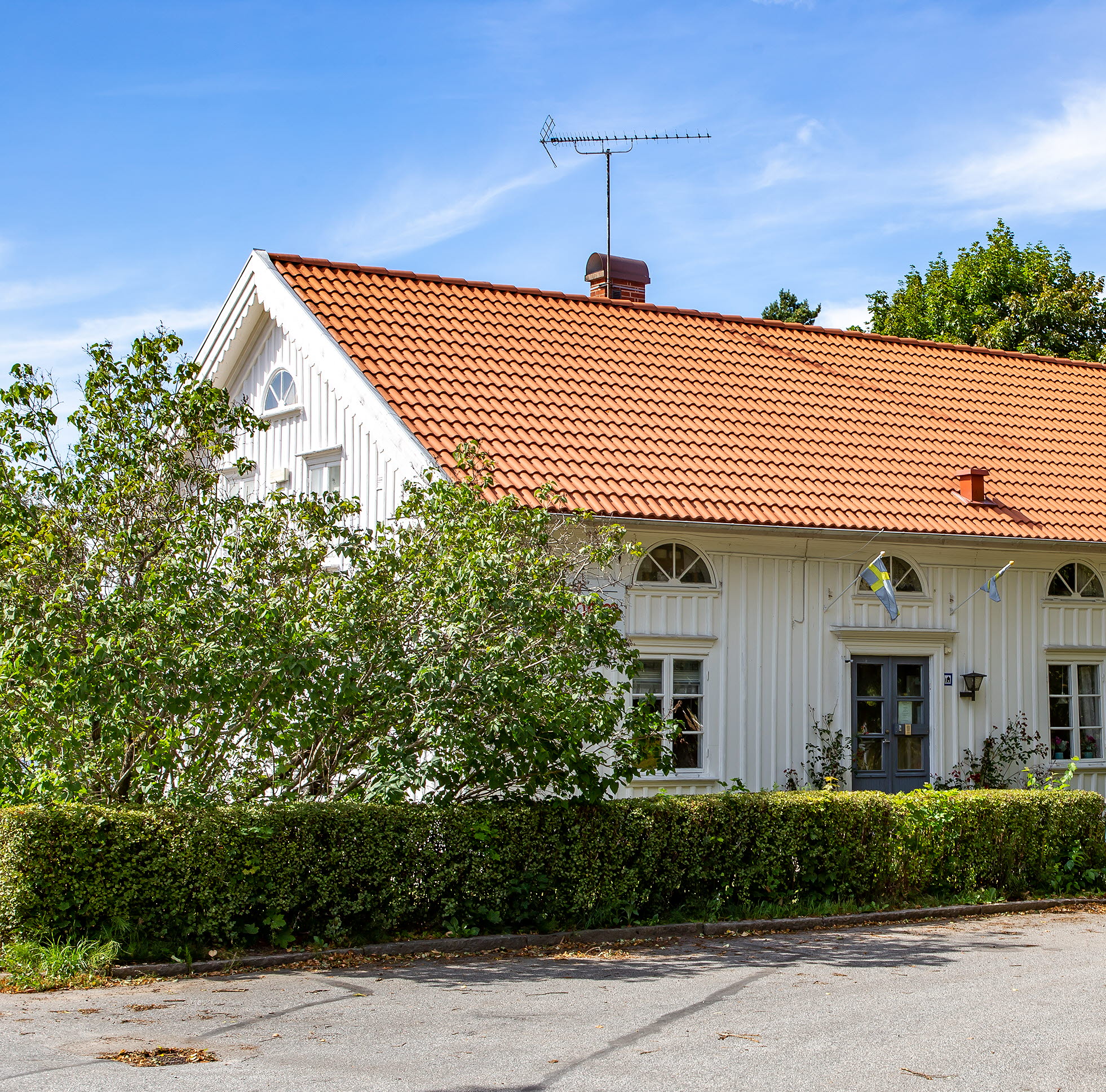 En bild på ett vackert vitmålat gammalt hus omgivet av gröna buskar.