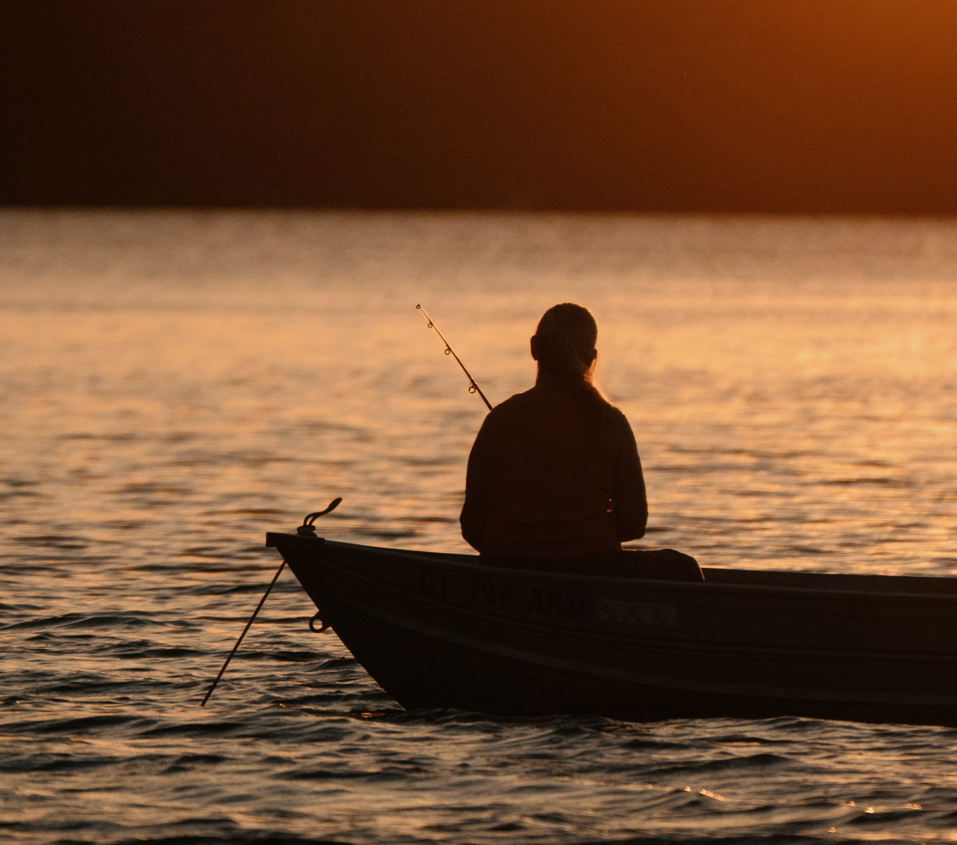 En bild på en man i en båt som fiskar i solnedgången.