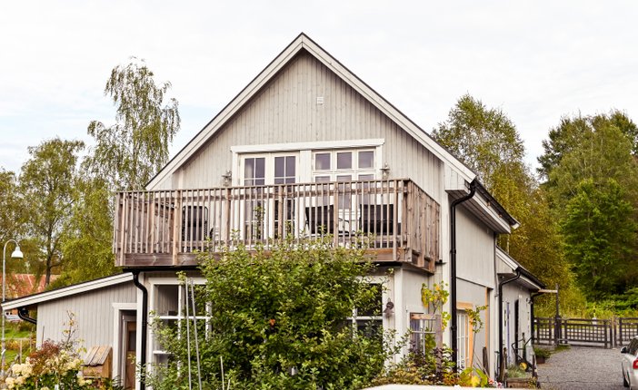 En bild på ett gråmålat hus med mycket buskar och grönska runtomkring