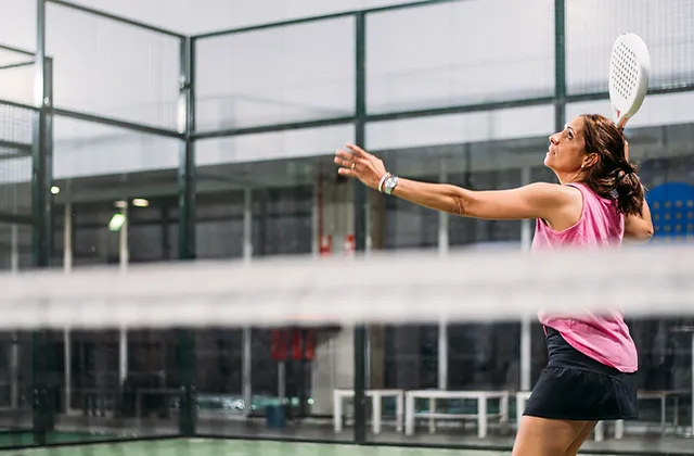 En bild på en kvinna som spelar padel på en inomhusbana.