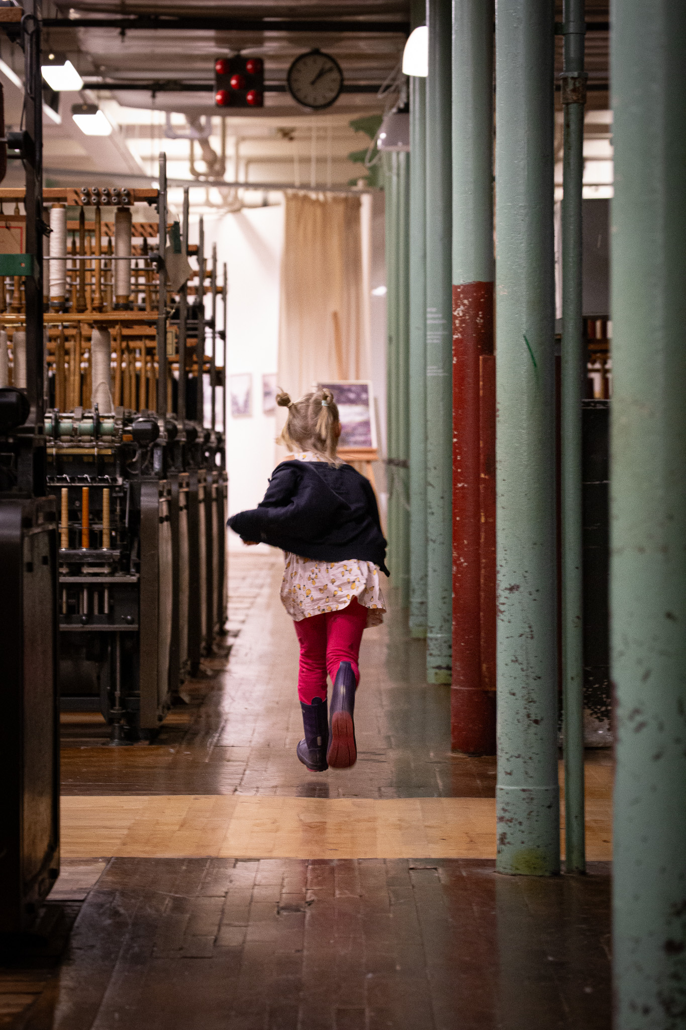 En bild på ett barn som springer över ett trägolv inne på en fabrik där spinnerimaskiner står uppradade.