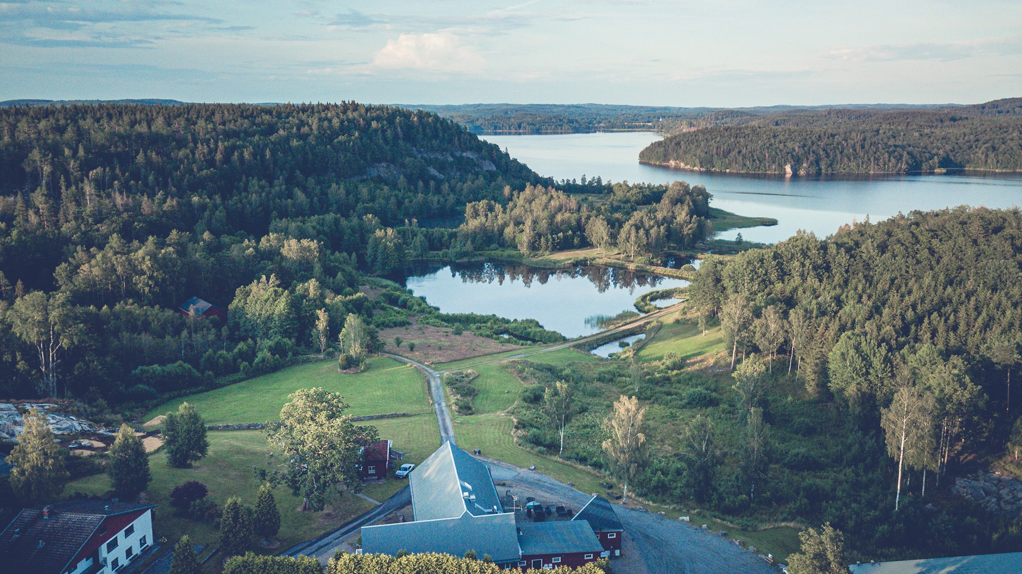 En bild tagen ovanifrån på en hotellverksamhet som ligger inbäddat i grönska framför en sjö.