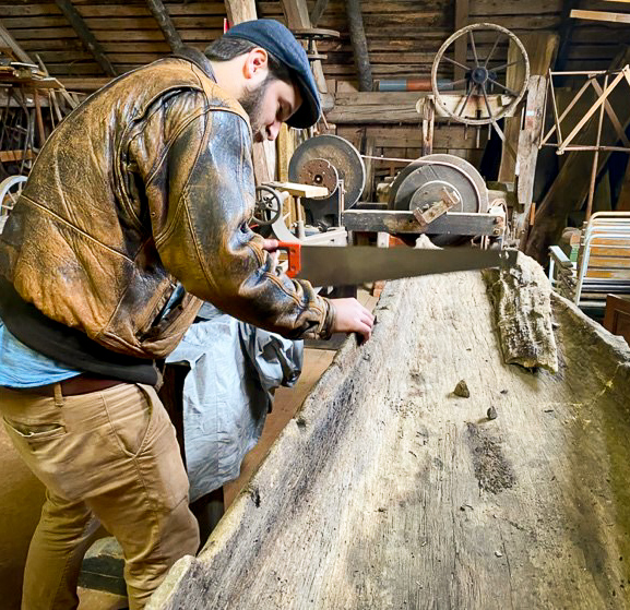 En bild på en man som står i en lada och sågar i en mycket gammal stockbåt