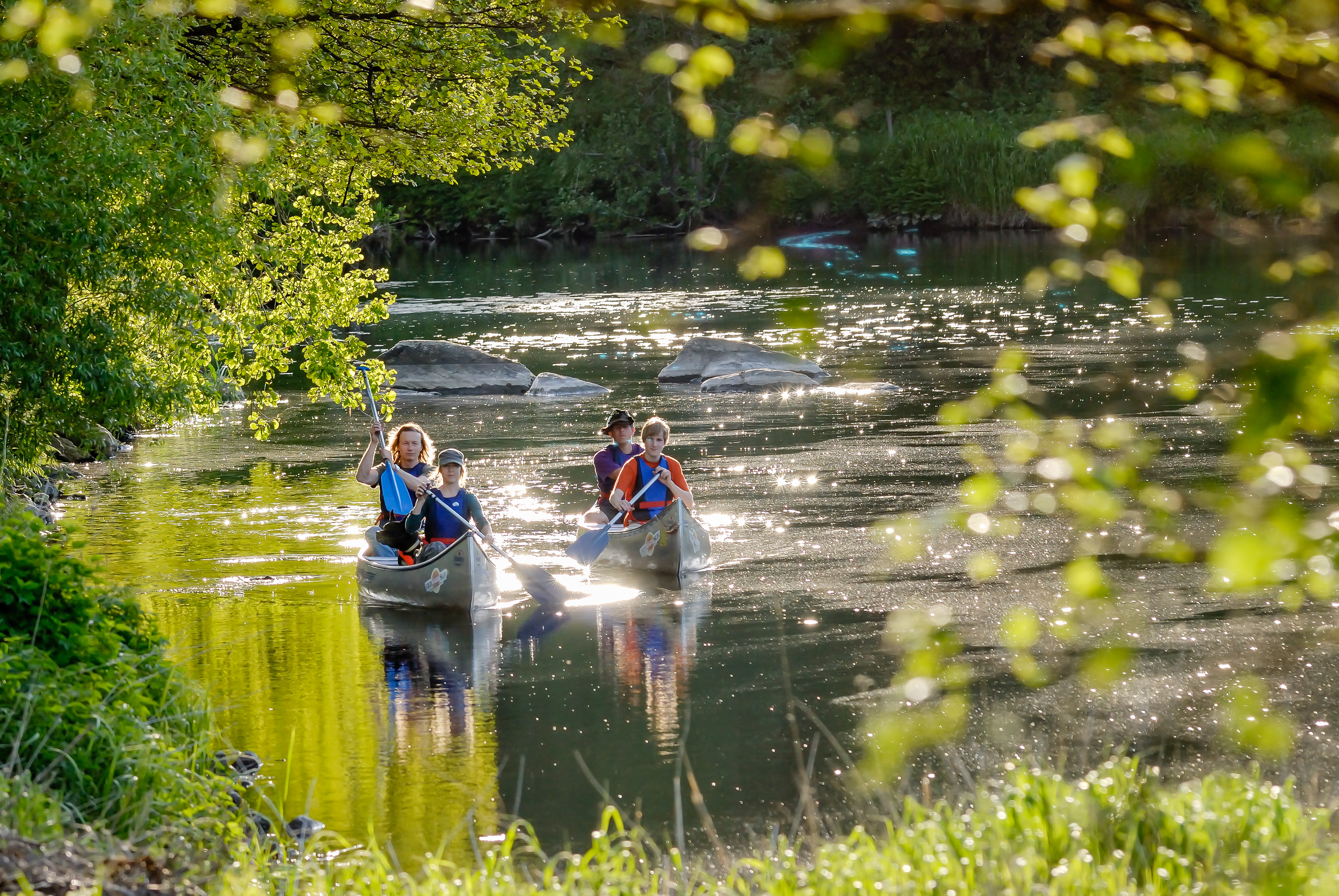 En bild på två kanoter som flyter på en glittrande å
