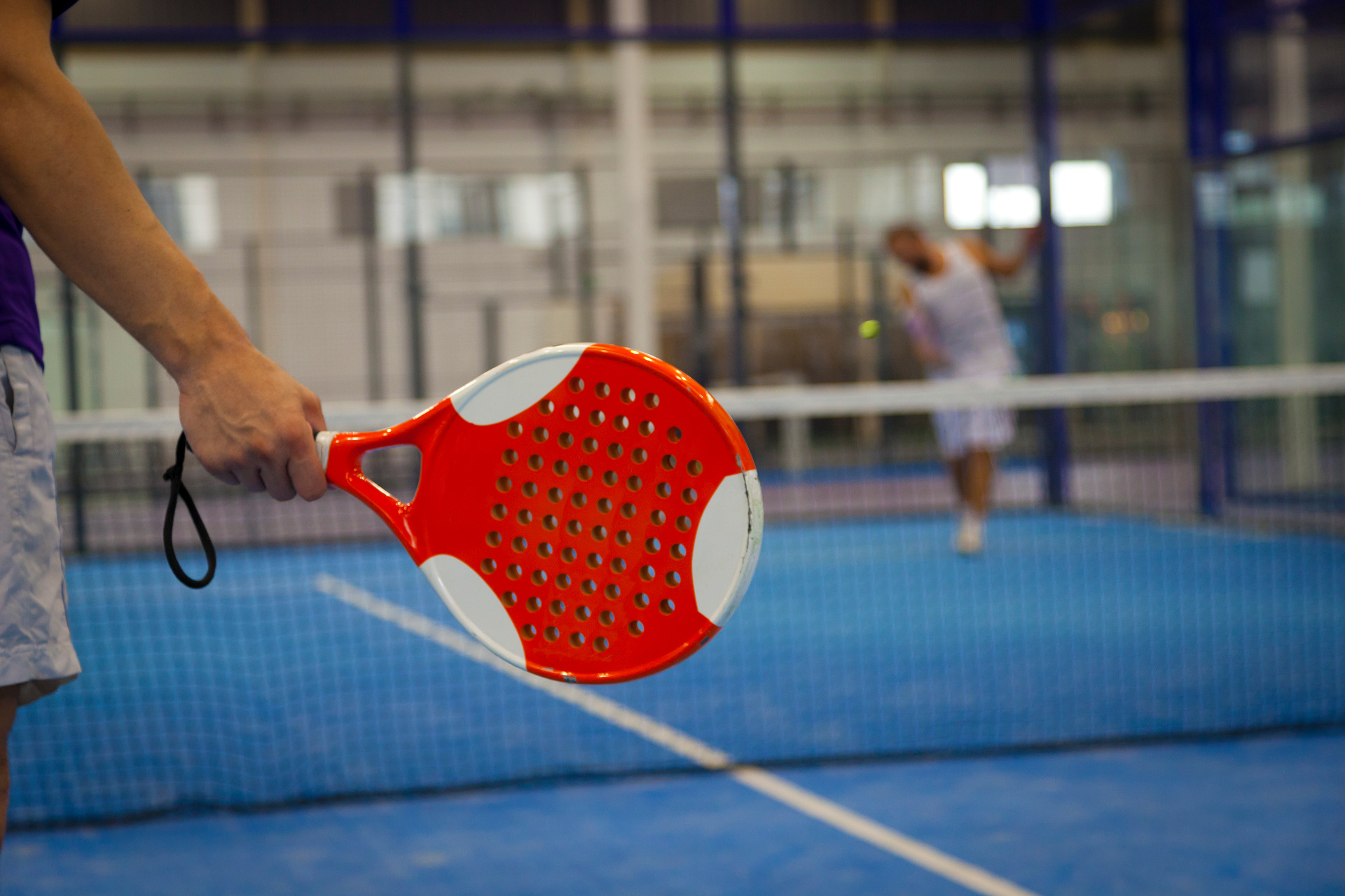 En bild på ett padelrack som någon håller i, i bakgrunden kan man skymta ett nät och en motspelare. 