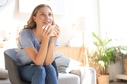 Kvinna sitter i ljus miljö och håller avslappnat i en kaffekopp.
