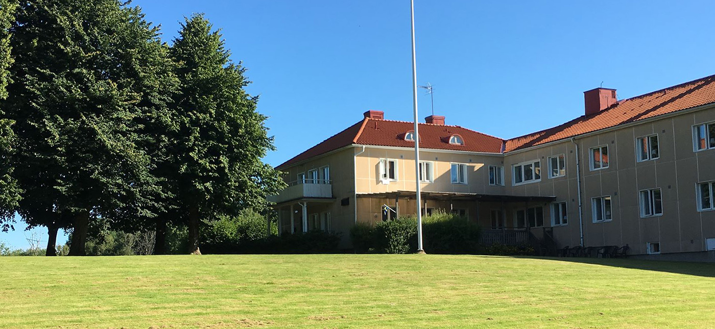 Exteriörbild av Partille vandrarhems byggnad med gul fasad och en grön gräsmatta framför och träd intill.