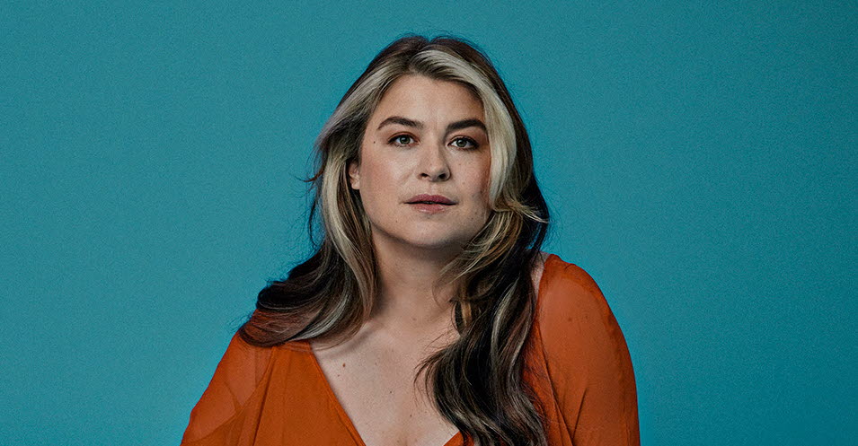 Linnea Henriksson sitter i en röd klänning mot en blå bakgrund.