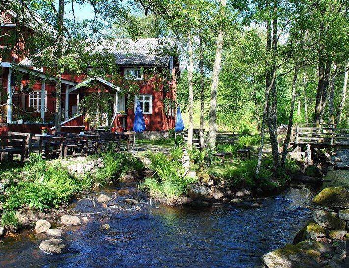 Vänga kvarn från utsidan. En röd byggnad med vita knutar och en bäck som rinner bredvid.