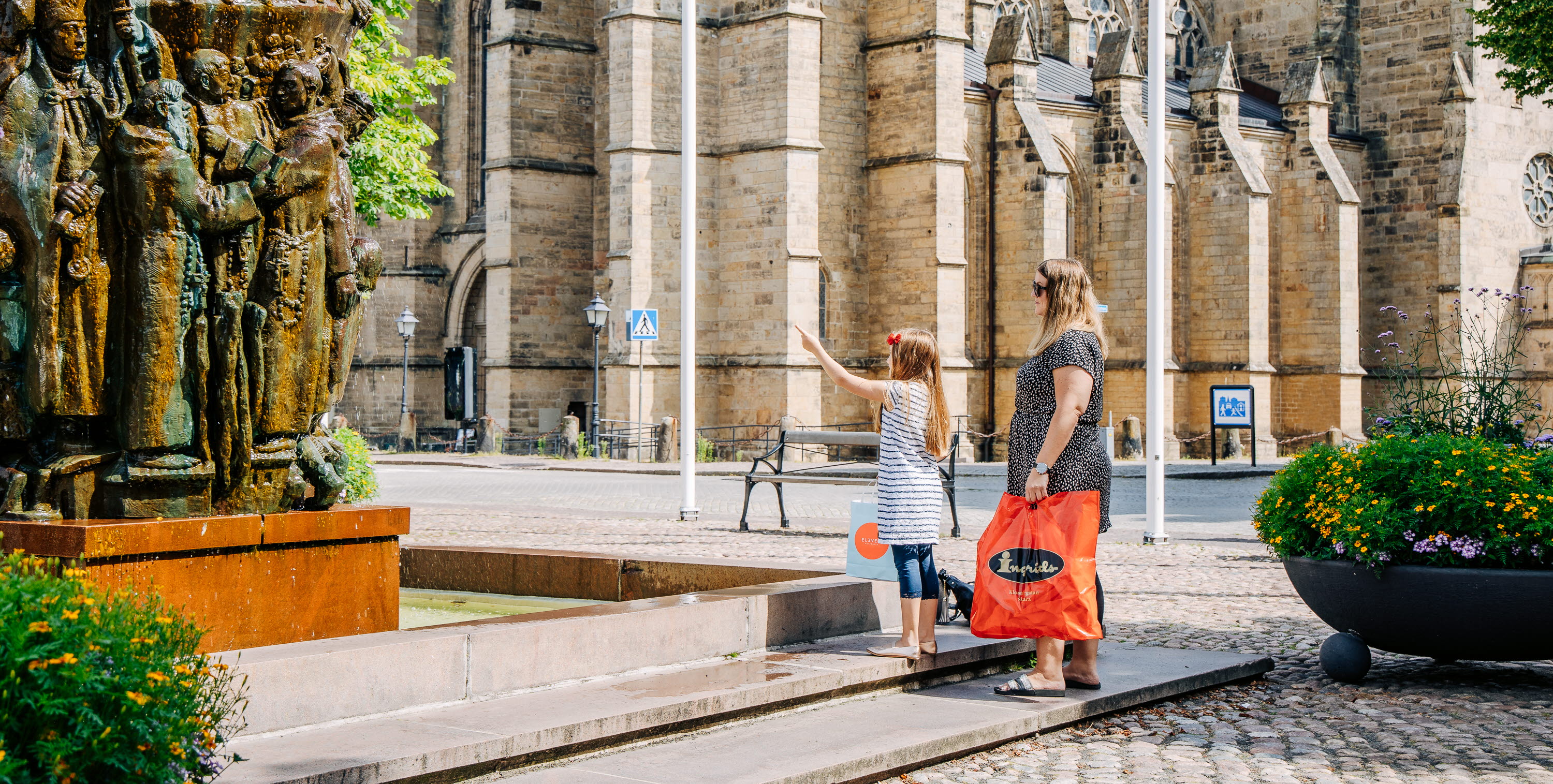 Två personer tittar på Krönikebrunnen vid Stortorget i Skara