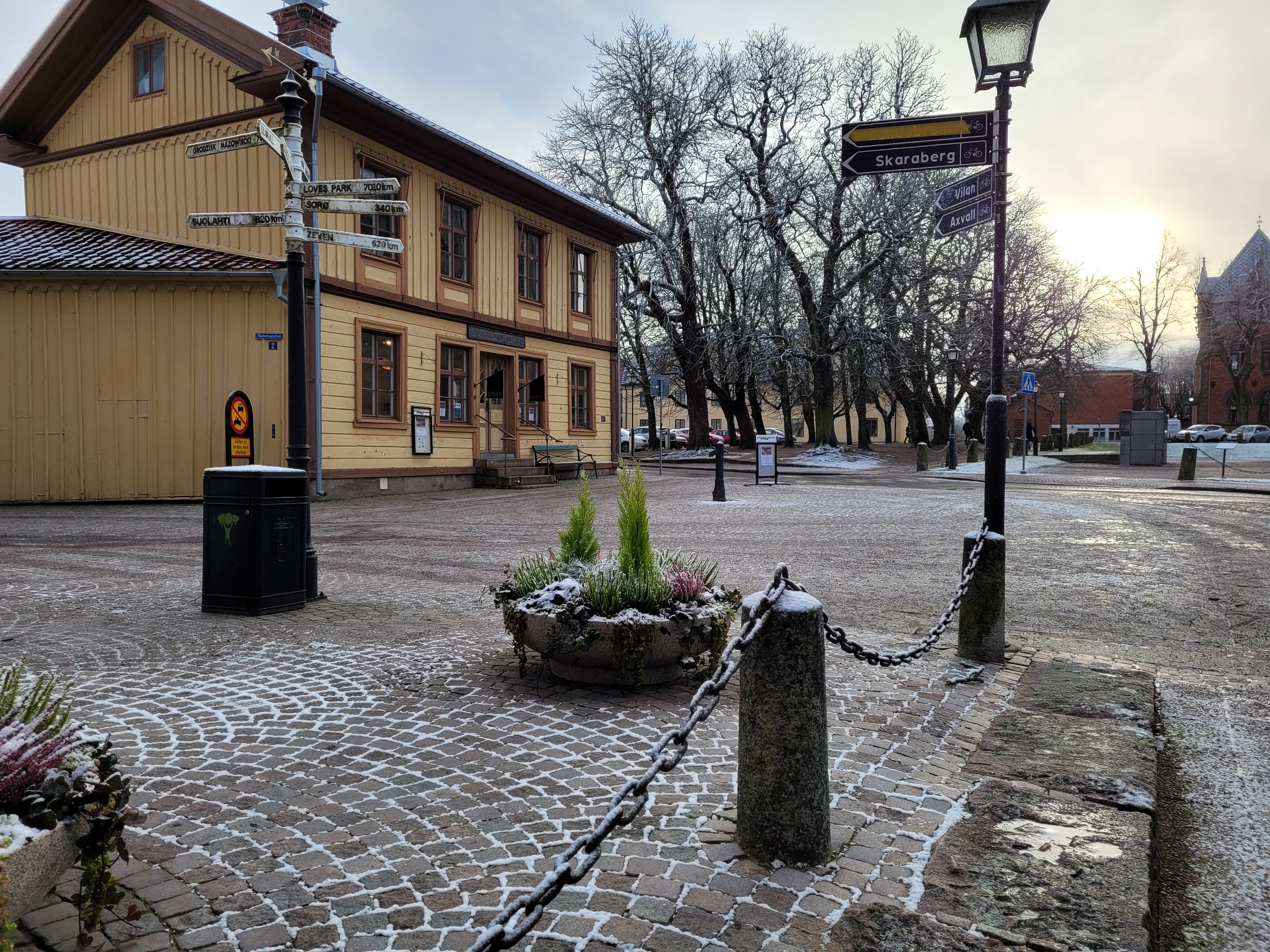 Ett gult trähus ligger intill ett litet torg av gatsten.
