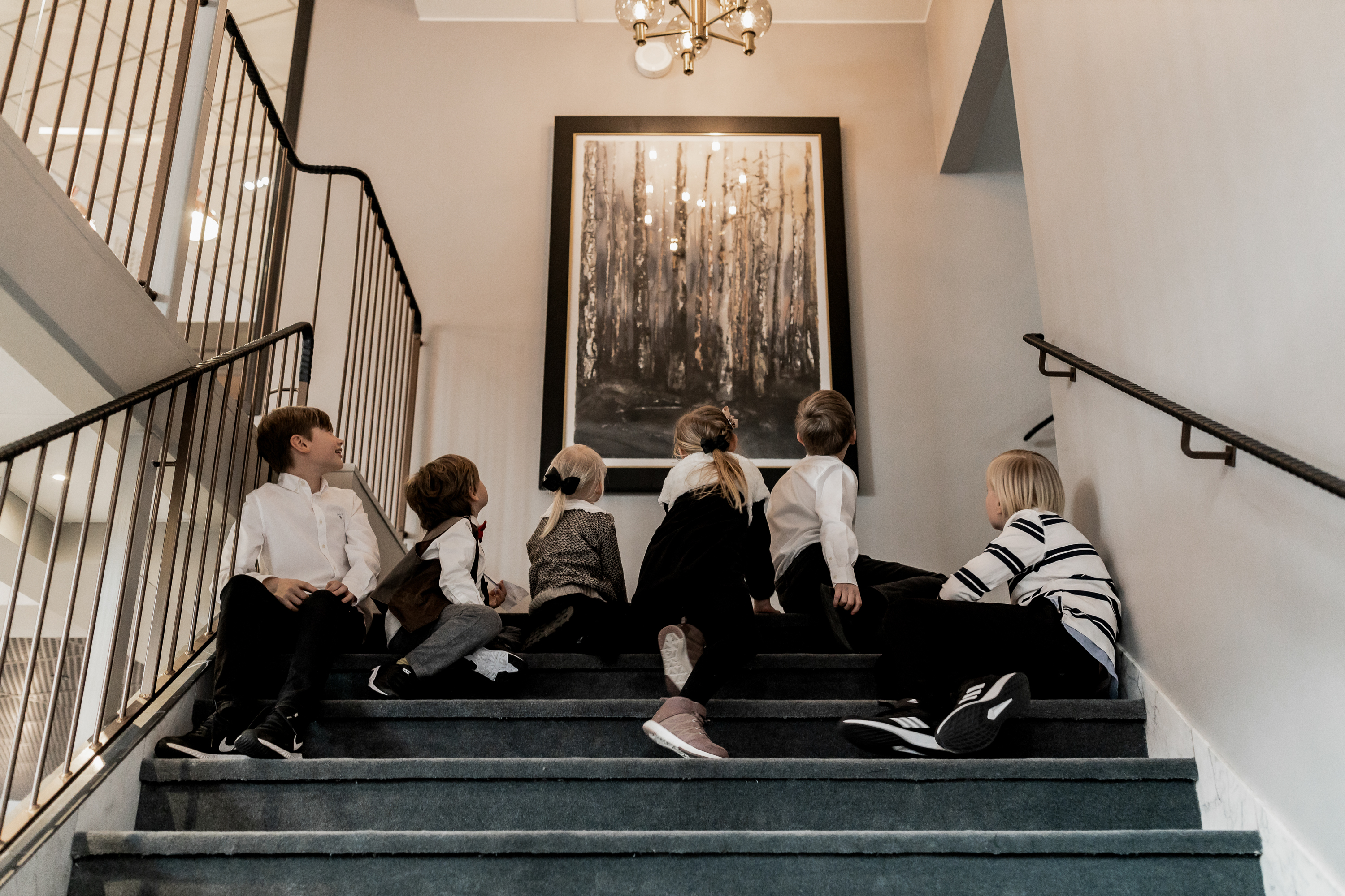 Sex barn sitter i en trappa och tittar på en stor tavla.