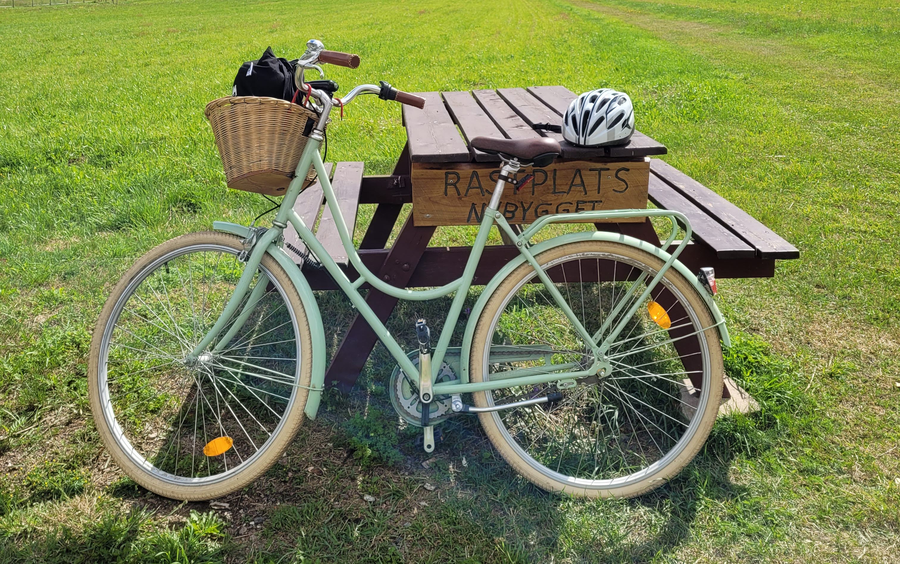 En grön cykel står lutad mot ett picknickbord. På bordet sitter en skylt med texten "Rastplats nybygget".