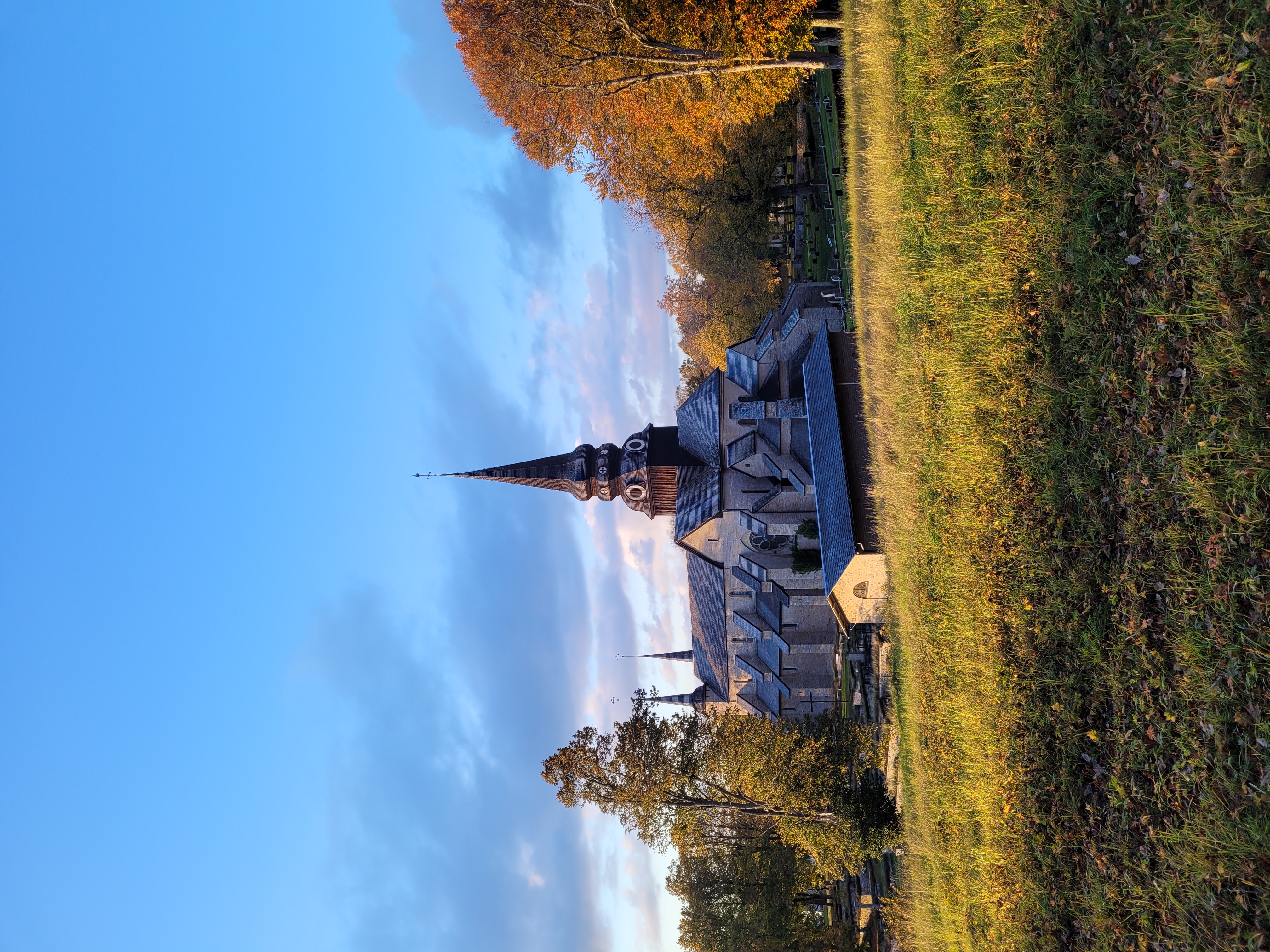 Varnhems klosterkyrka i höstskrud. Gräset är grönt men träden börjar färgas orange.