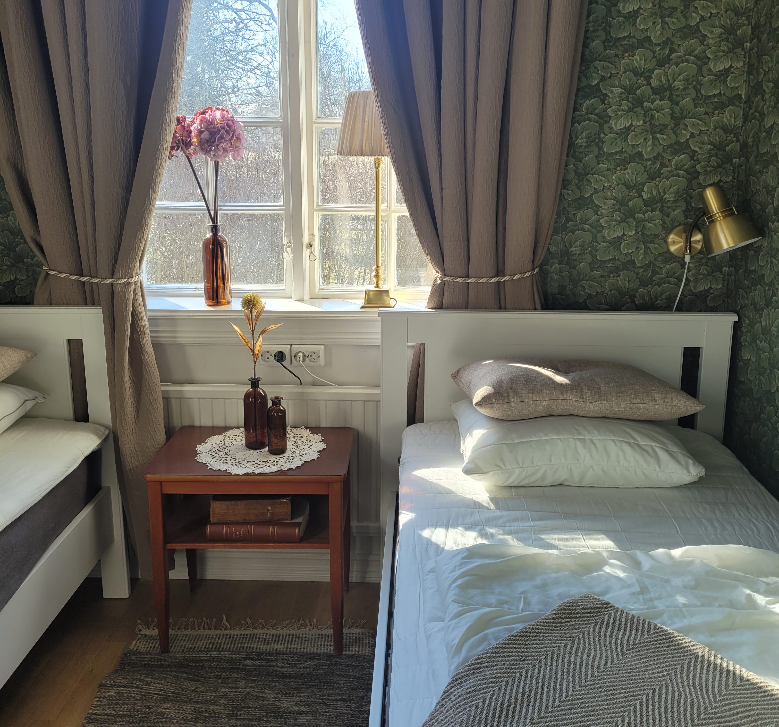 Två sängar i ett rum. Mellan sängarna står ett litet nattygsbord med två bruna glasvaser. 