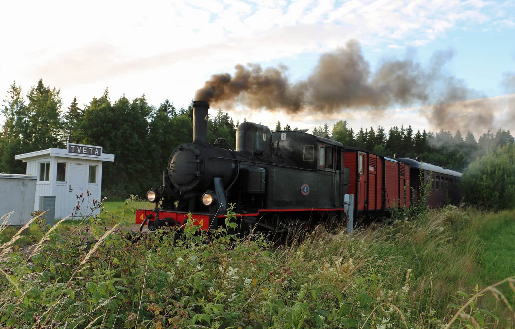 Ett svart ånglok åker förbi en vit kur med  en skylt med texten TVETA.