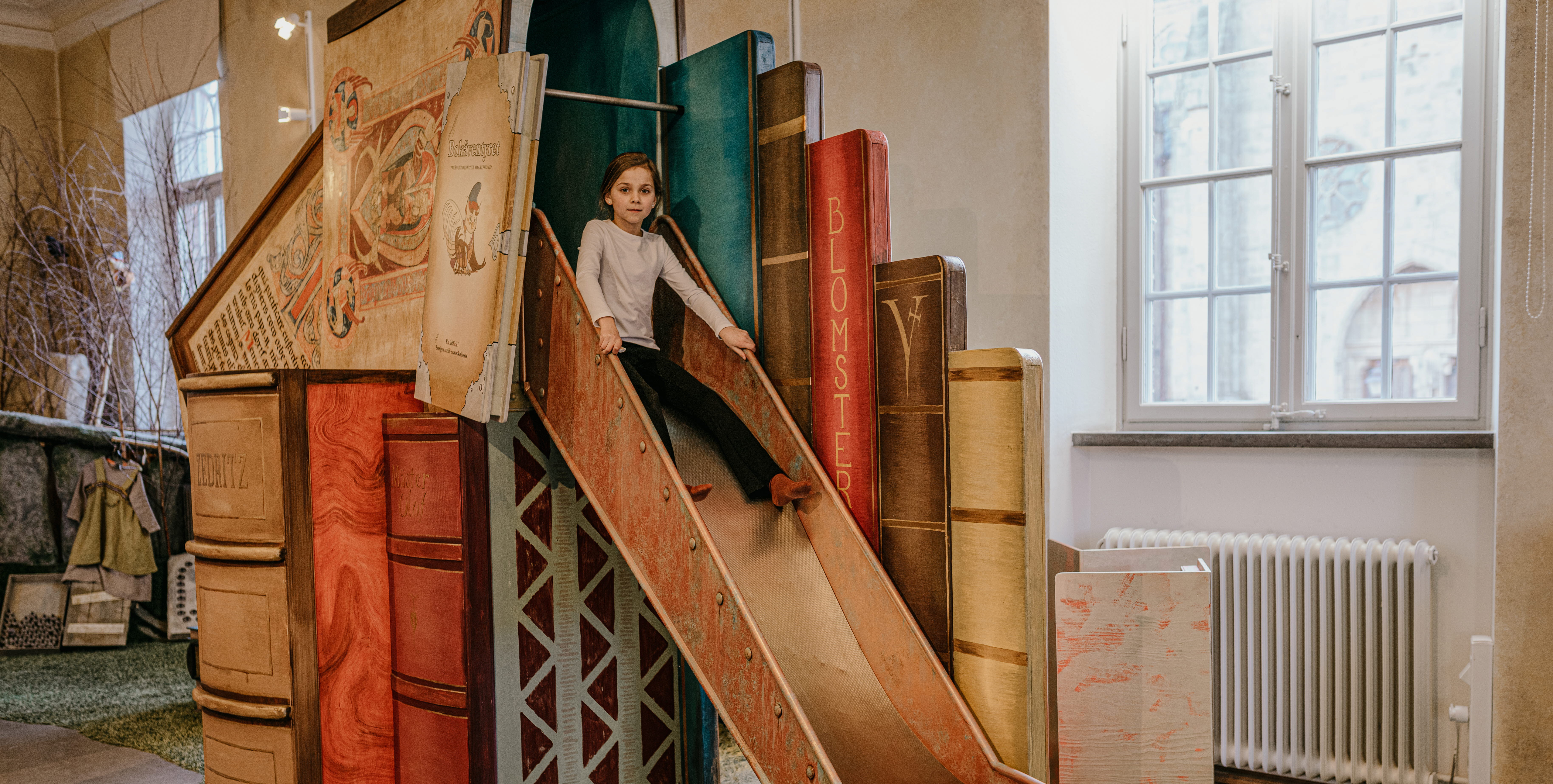 Bokäventyret. Barn åker ner för rutschkana.  