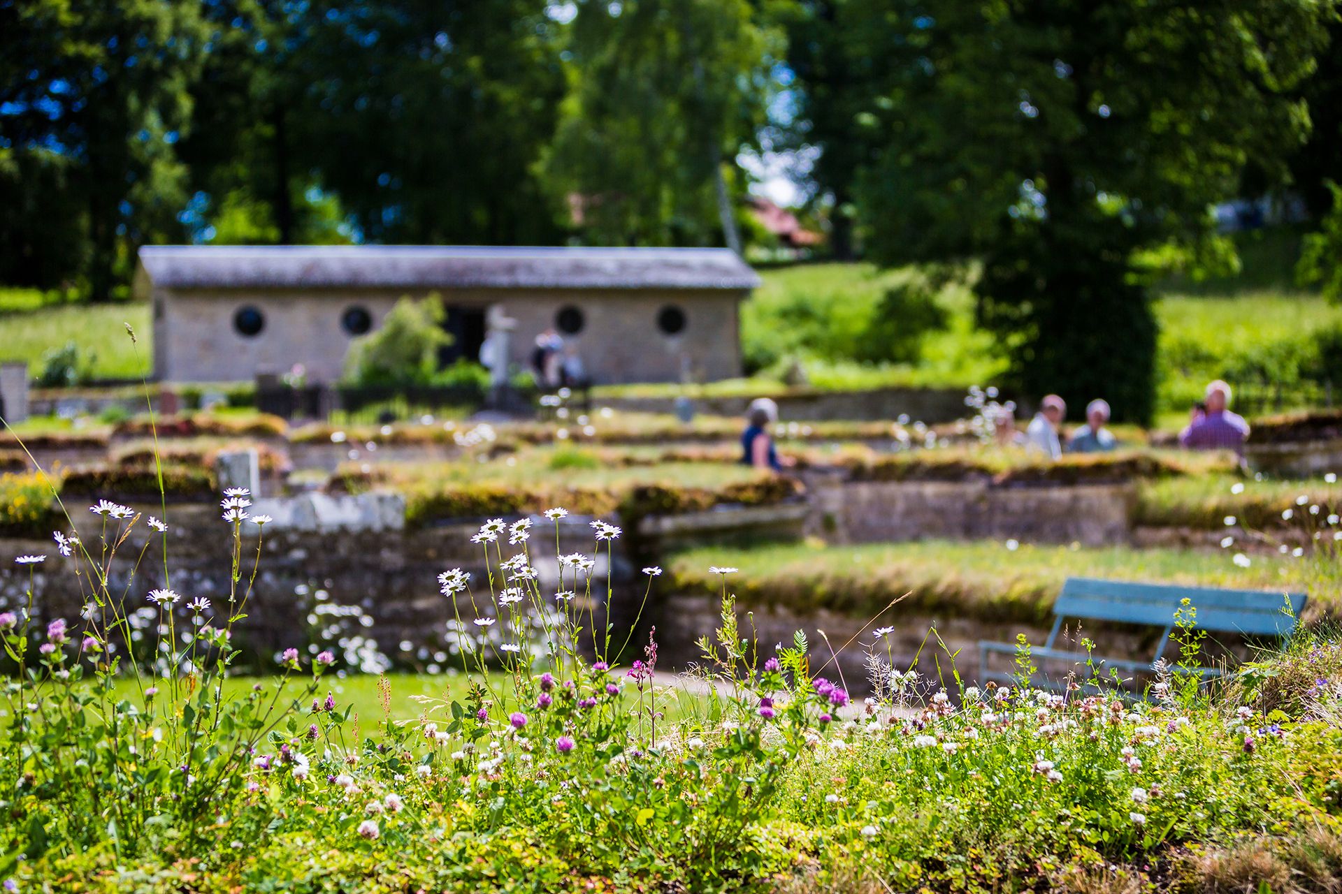 Människor står utomhus sommartid framför en tegelbyggnad med grönska runt omkring.