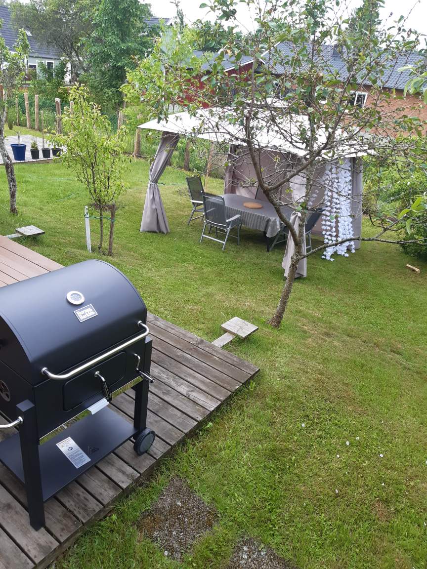 Utemöbler under ett partytält samt en grill i en trädgård.