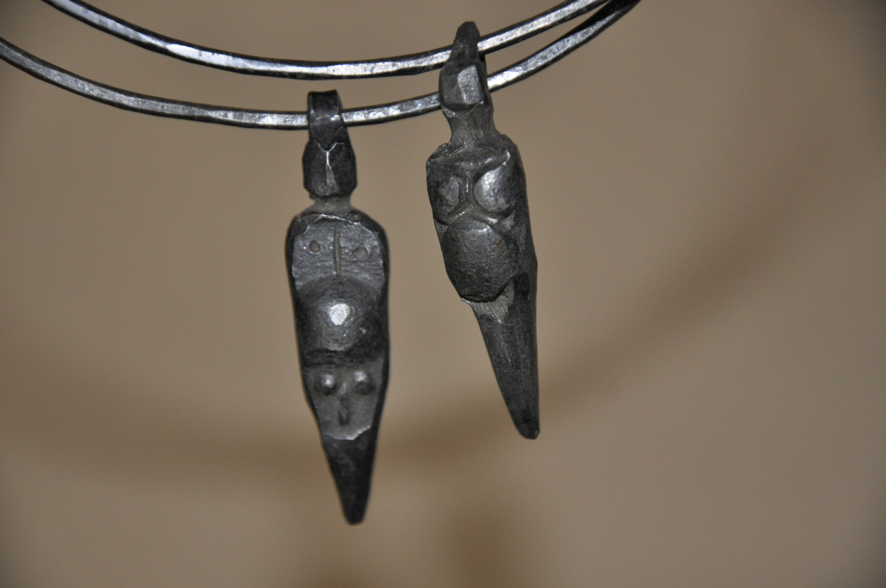 Två berlocker i metall, föreställande två stiliserade människokroppar hänger på varsin järnring.