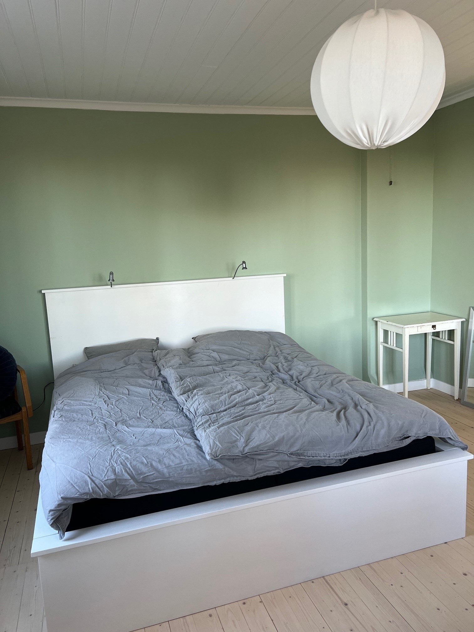 Ett sovrum med dubbelsäng och ljusgröna väggar.