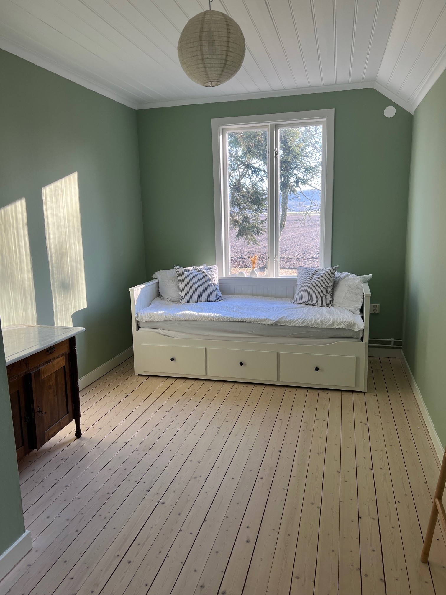 Ett sovrum med en bäddsoffa, gröna väggar och ljusa trägolv.