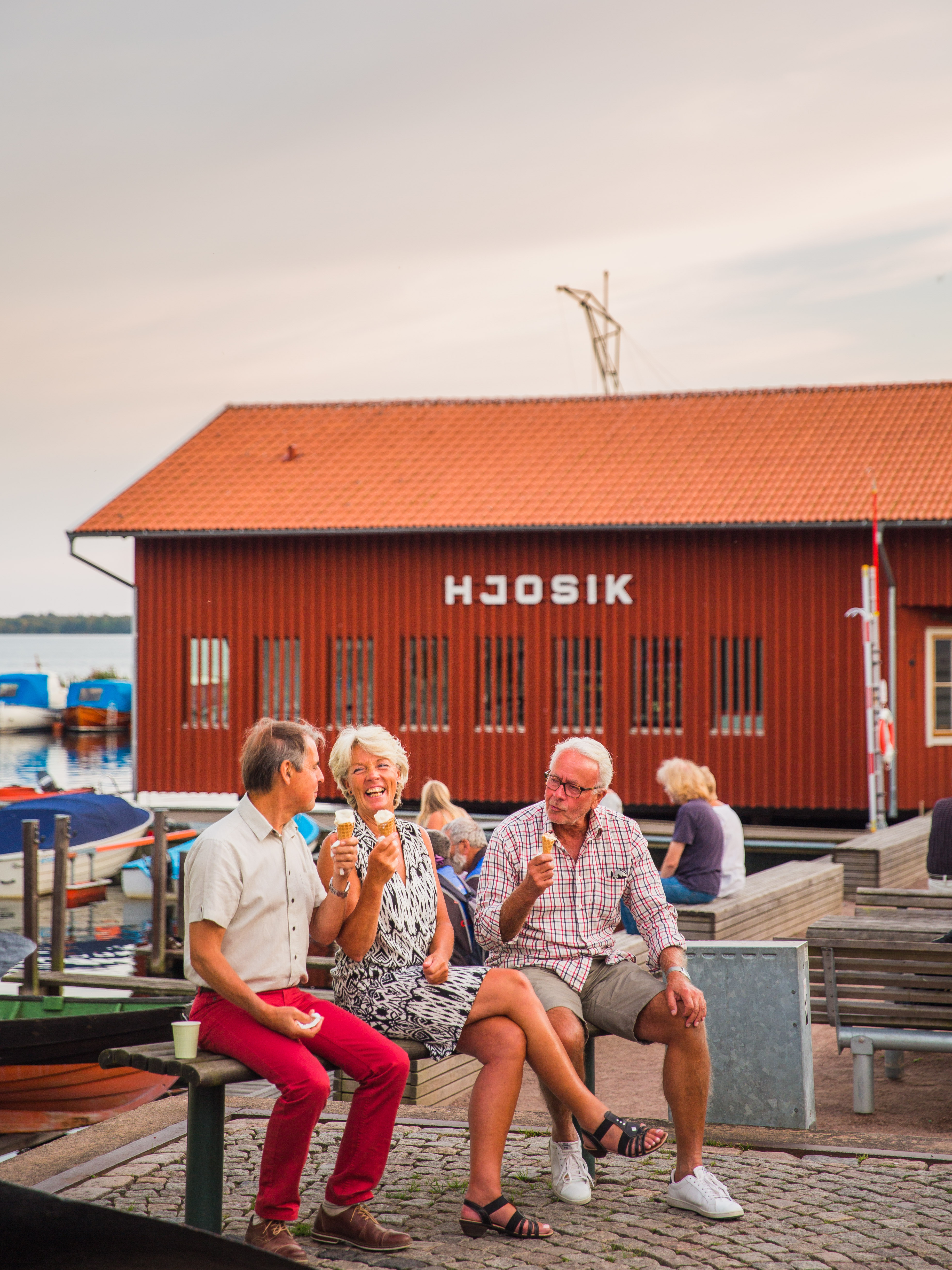Tre människor äter glass i Hjo hamn, med fiskaffären Hjo Sik i bakgrunden. 