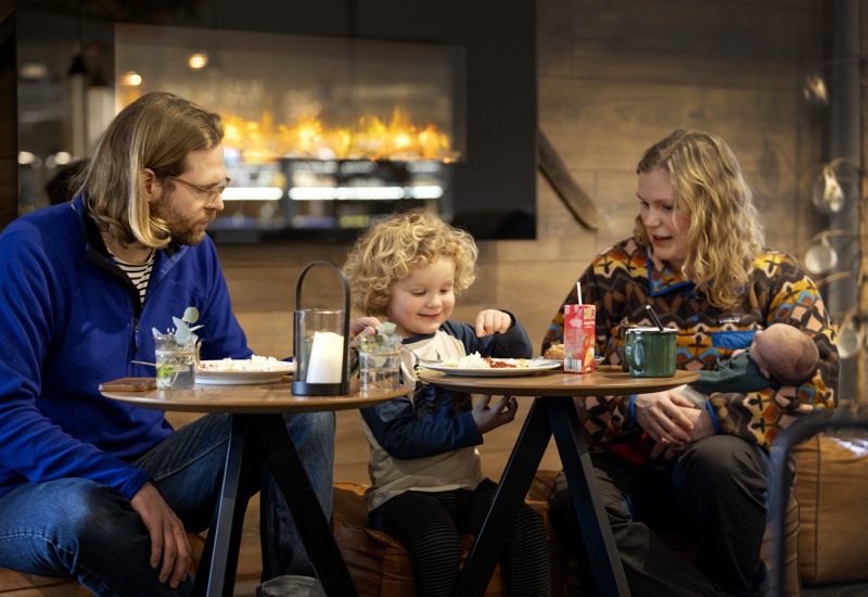 En familj sitter och fikar vid några bord.