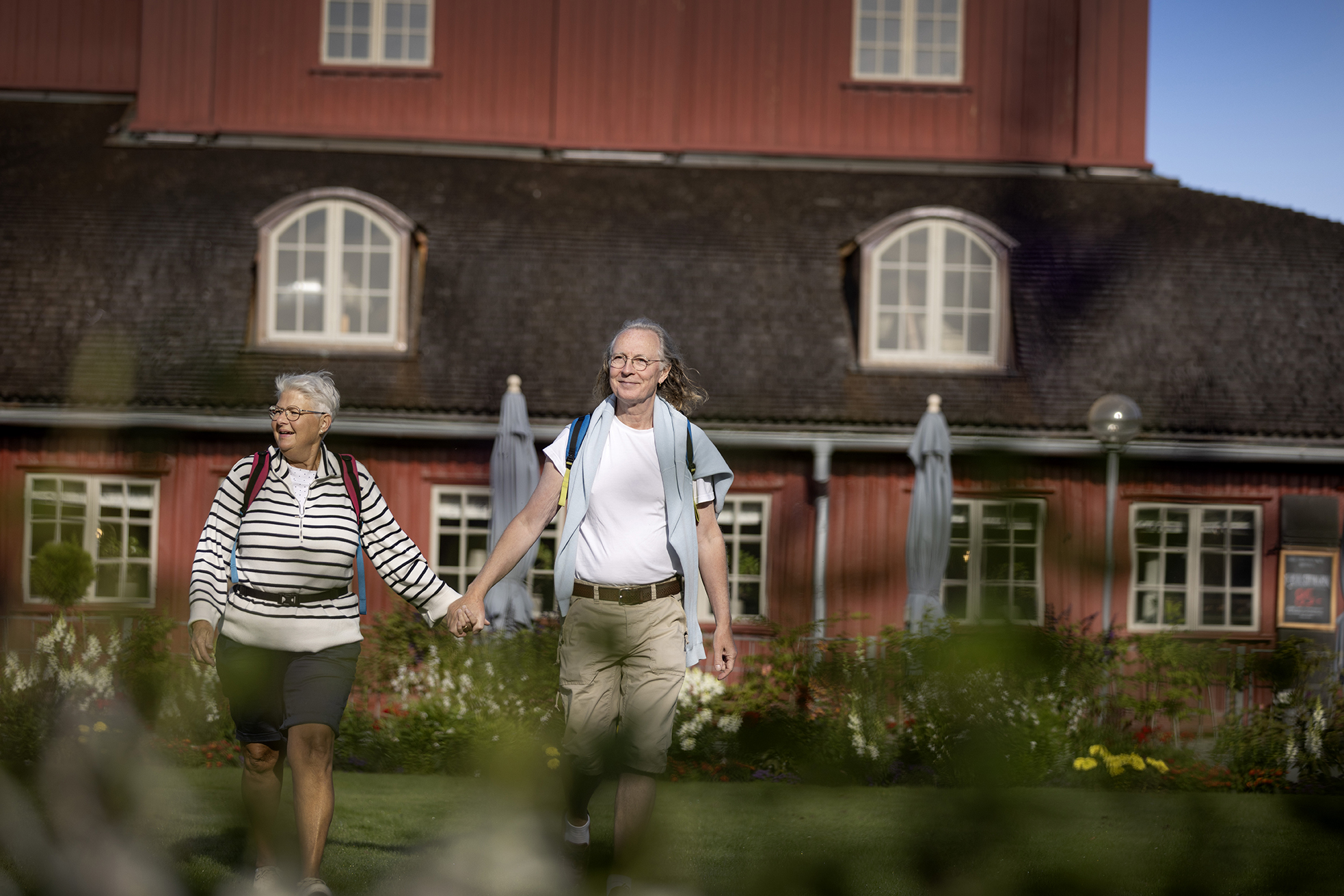 Ett äldre par håller varandra i handen framför en röd byggnad.