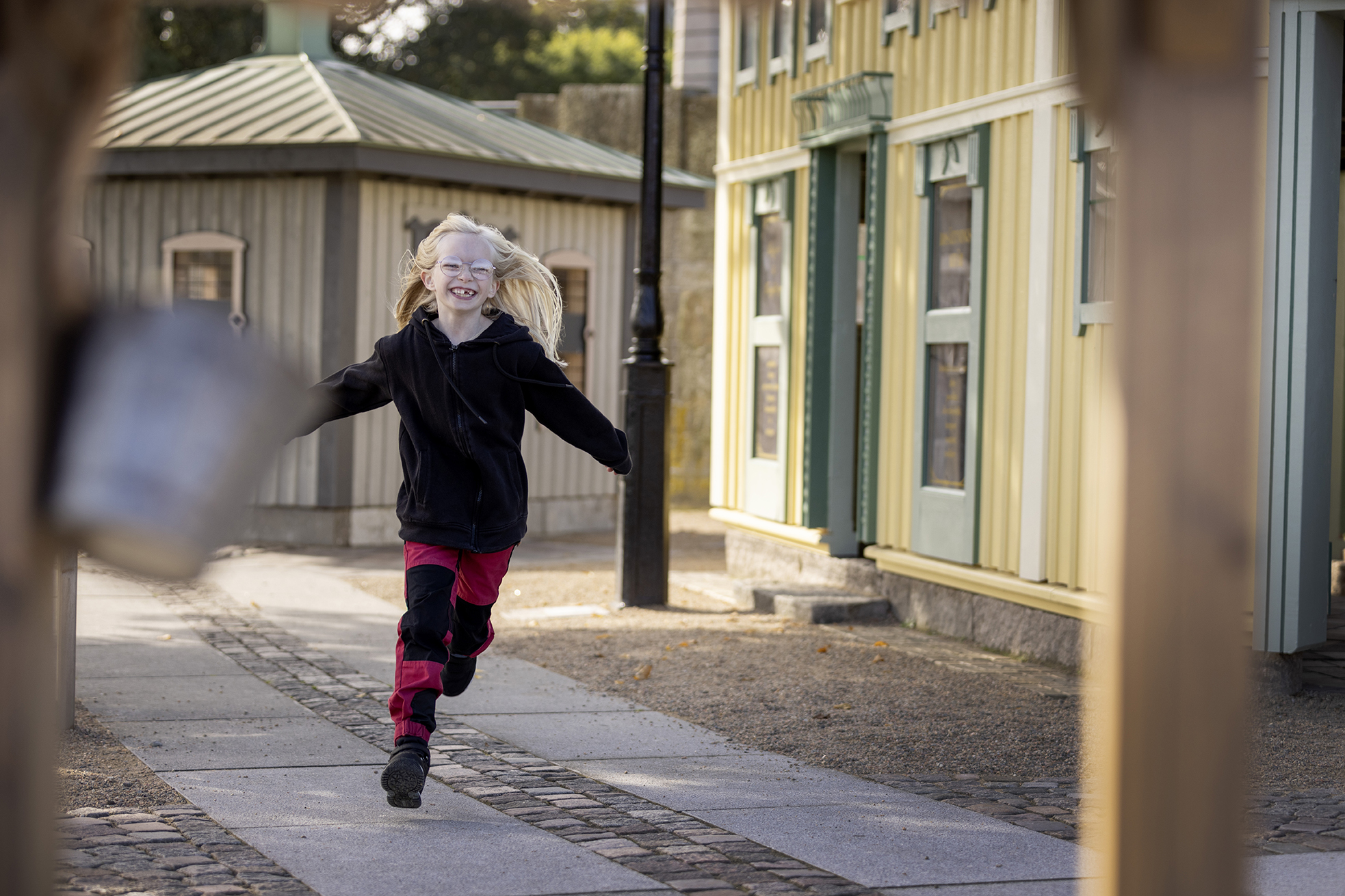 En glad tjej springer fram på en kullerstensgata det är gula byggnader bakom henne.