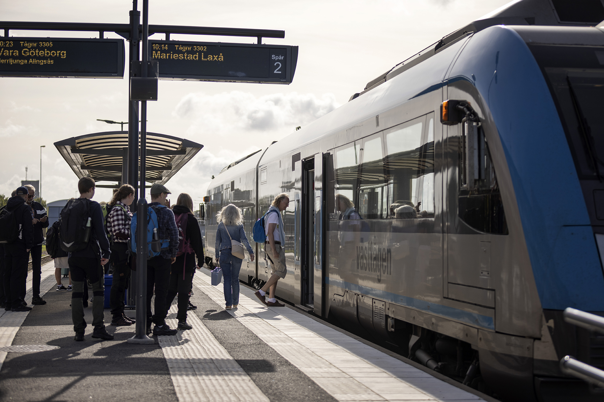 Människor står och väntar på att få gå ombord på ett väntande tåg.