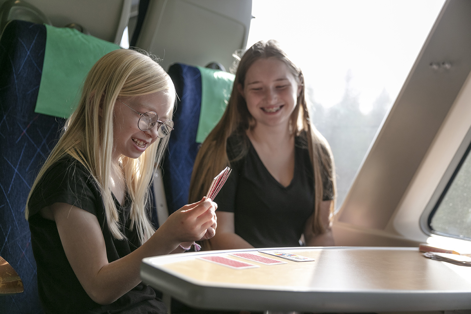 Två tjejer spelar kort på ett tåg.