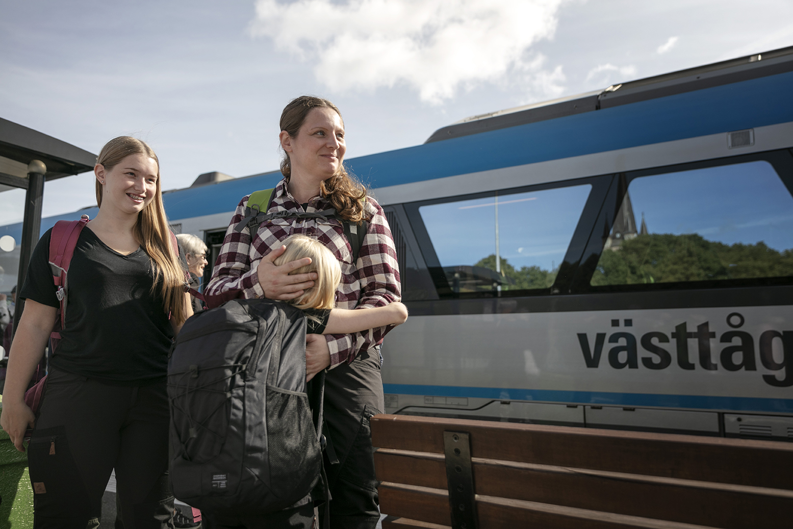 En kvinna med sina två döttrar står utanför ett tåg.