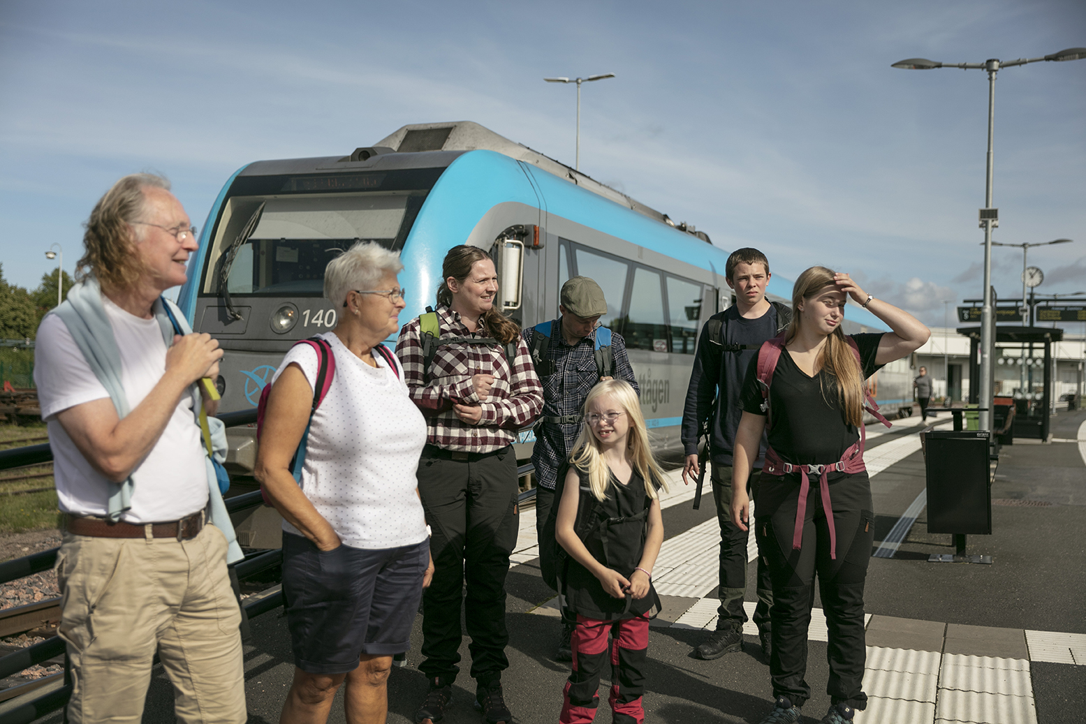 Ett äldre par och en familj med tre stycken barn står utanför ett tåg och tittar på något åt höger.