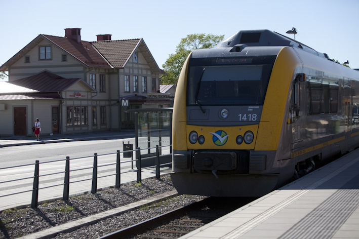 Tåg som står i station med en äldre stationsbyggnad i bakgrunden