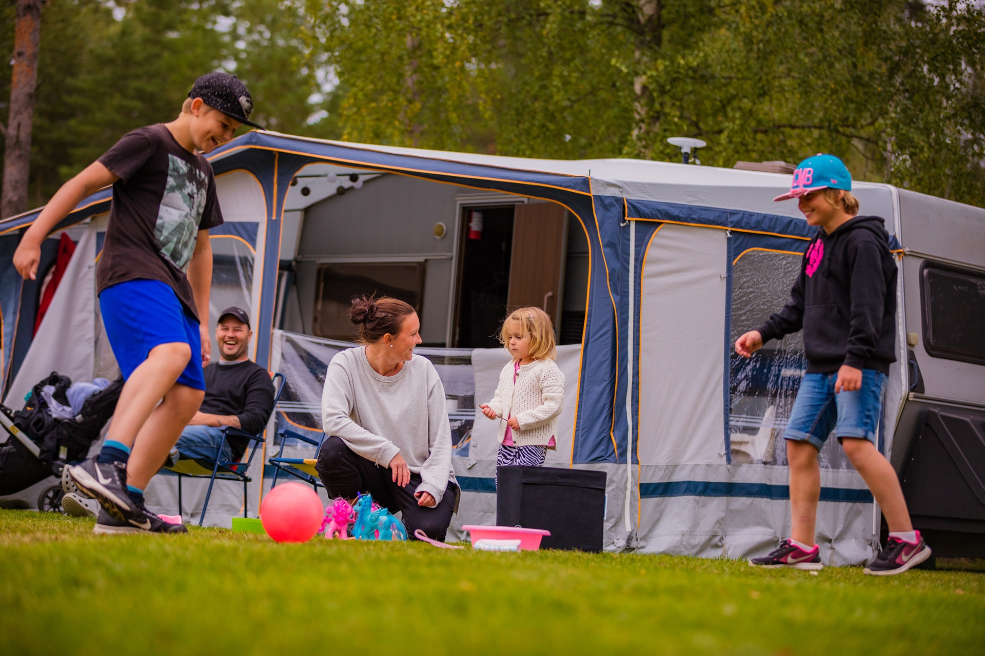 Husvagn med förtält på Skara Sommarlands camping. Flera personer sitter utanför och två personer spelar boll.