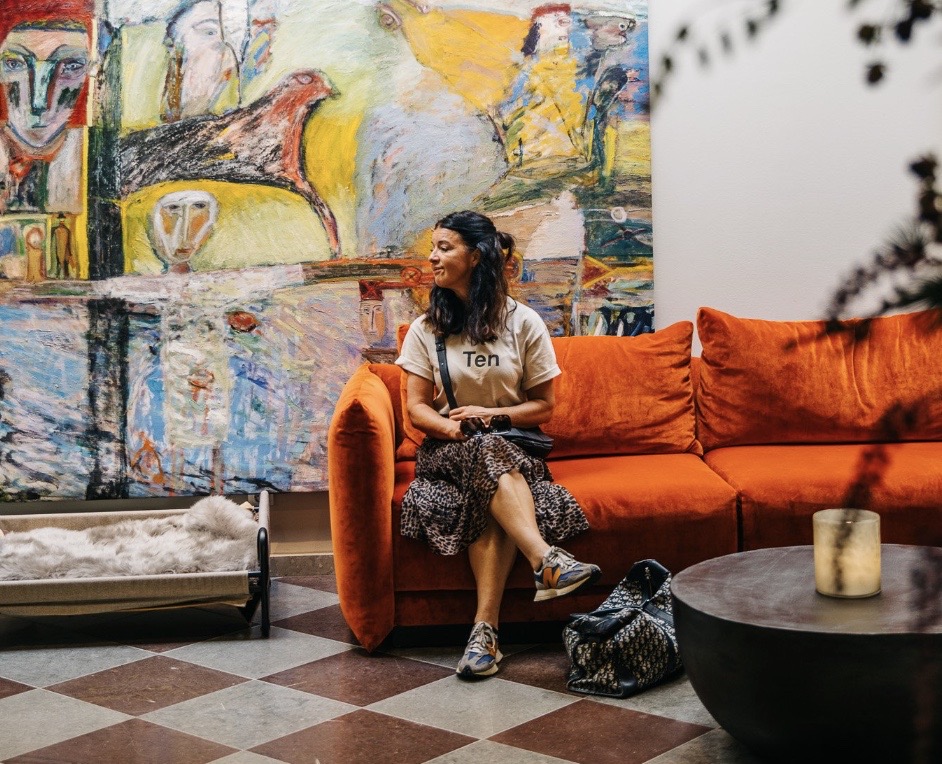 En kvinna sitter i en orange soffa med ett konstverk på väggen bakom.