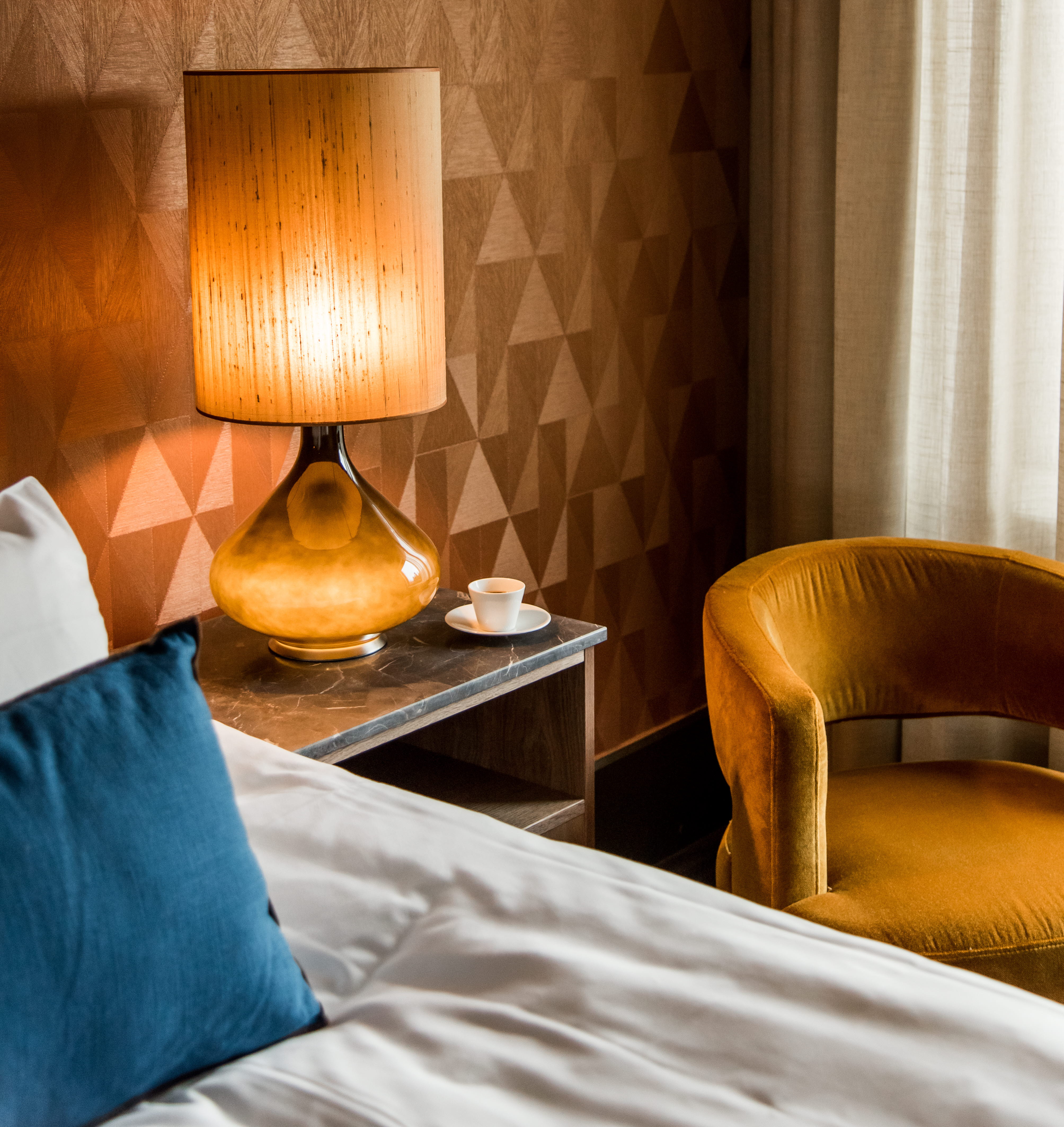 A hotel room with a bedside table with a large lamp
