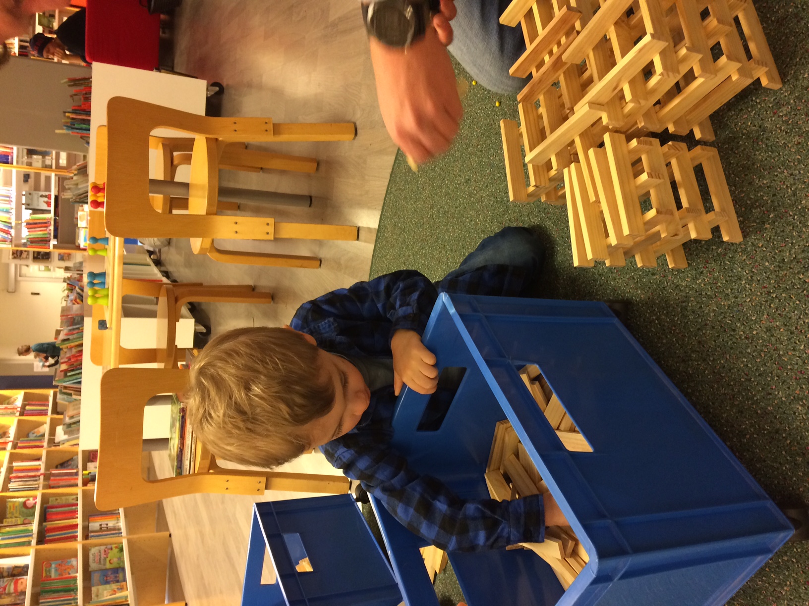 En pojke sitter på golvet i ett biblioteksrum och letar efter klossar i en blå plastback.