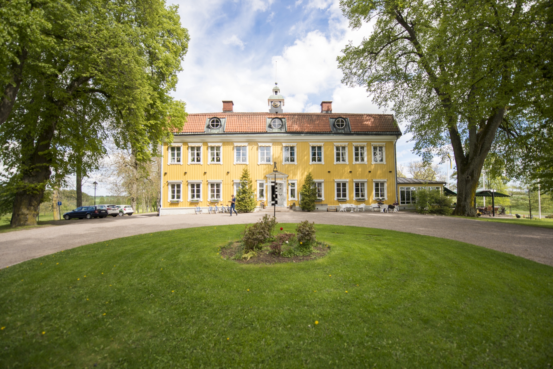 En gul herrgårdsbyggnad med en stor gräsyta framför