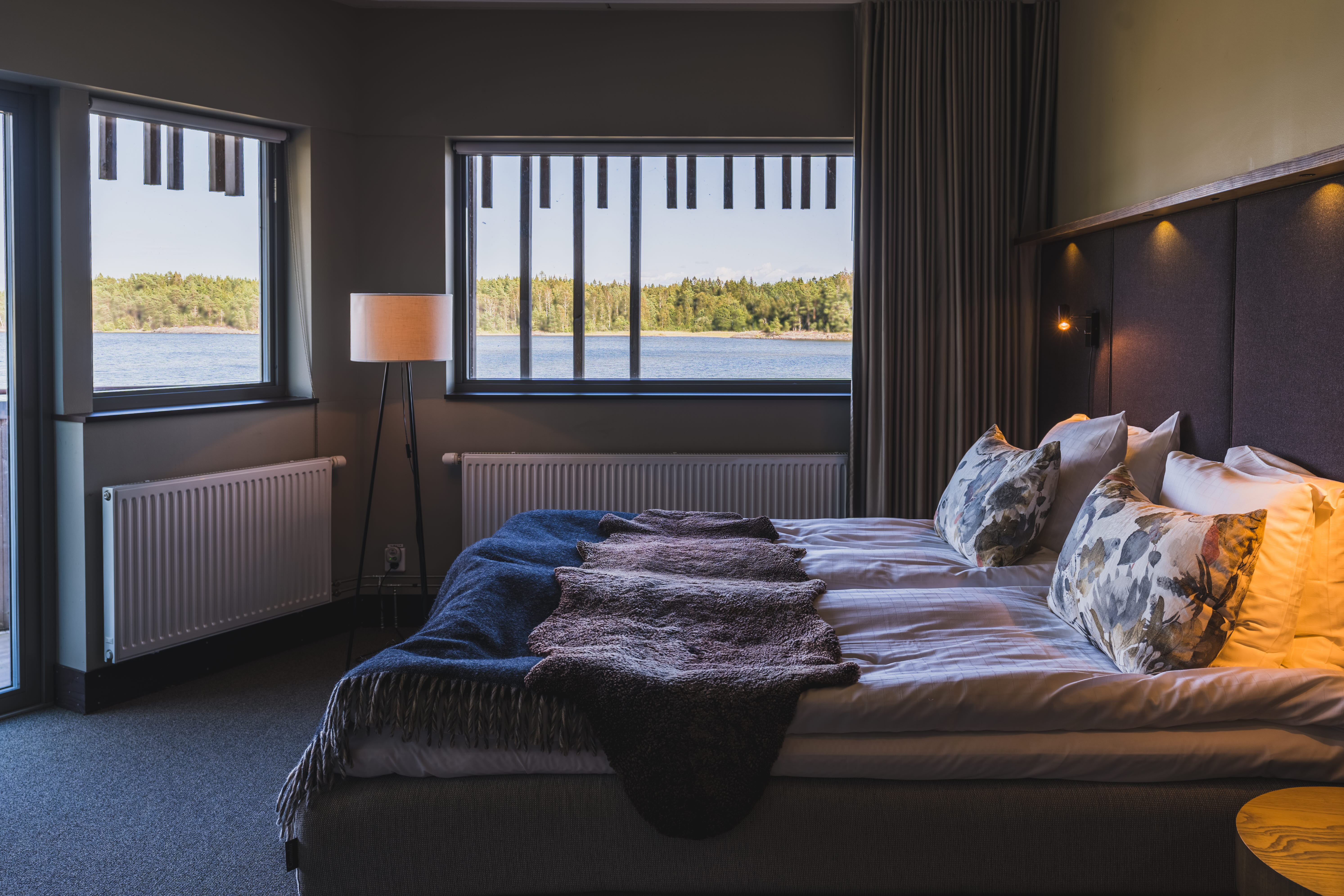 Ett hotellrum med en dubbelsäng och utsikt över en sjö genom två fönster.