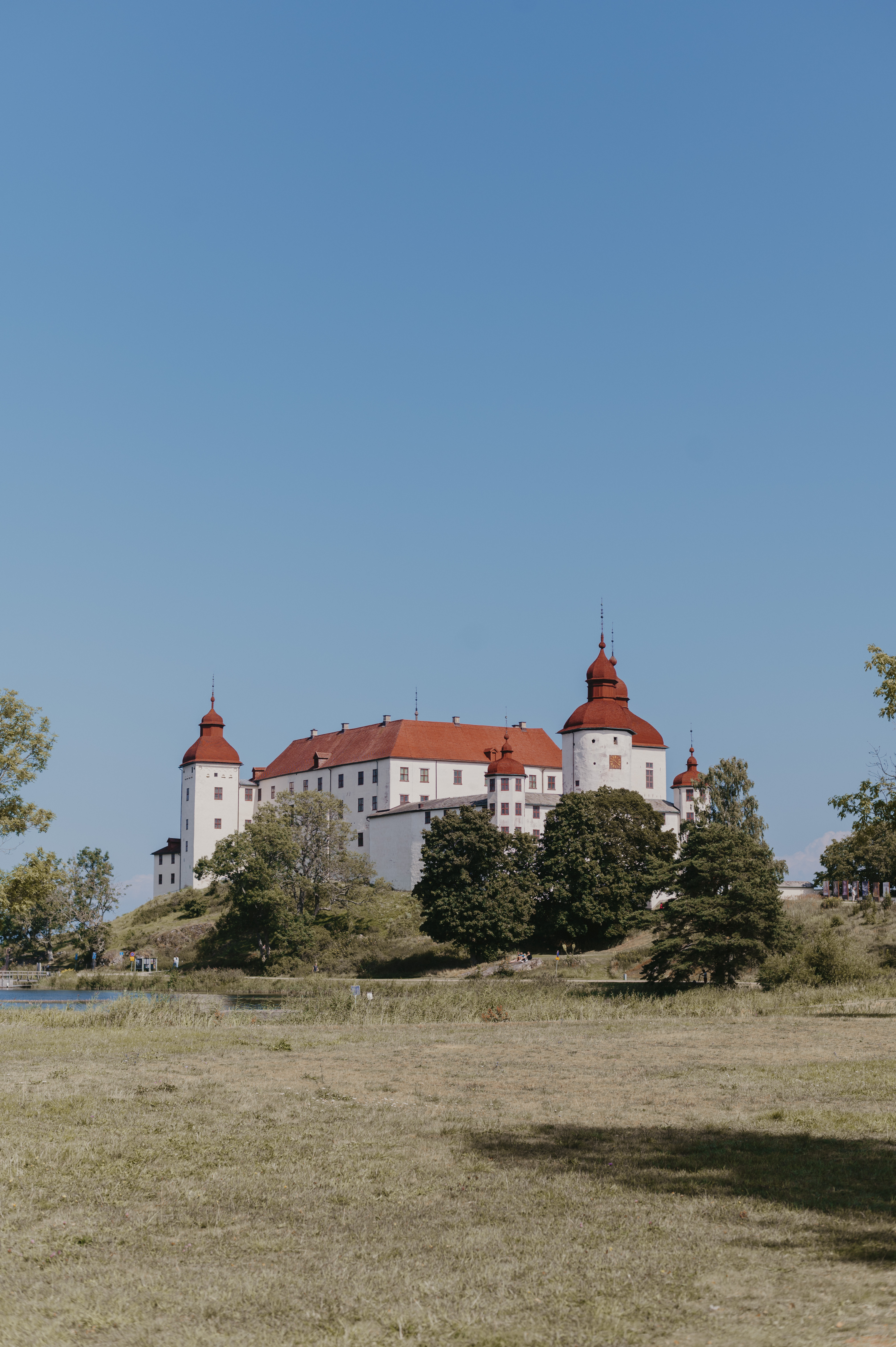 Ett vitt slott med rött tak och med grönskande träd framför.