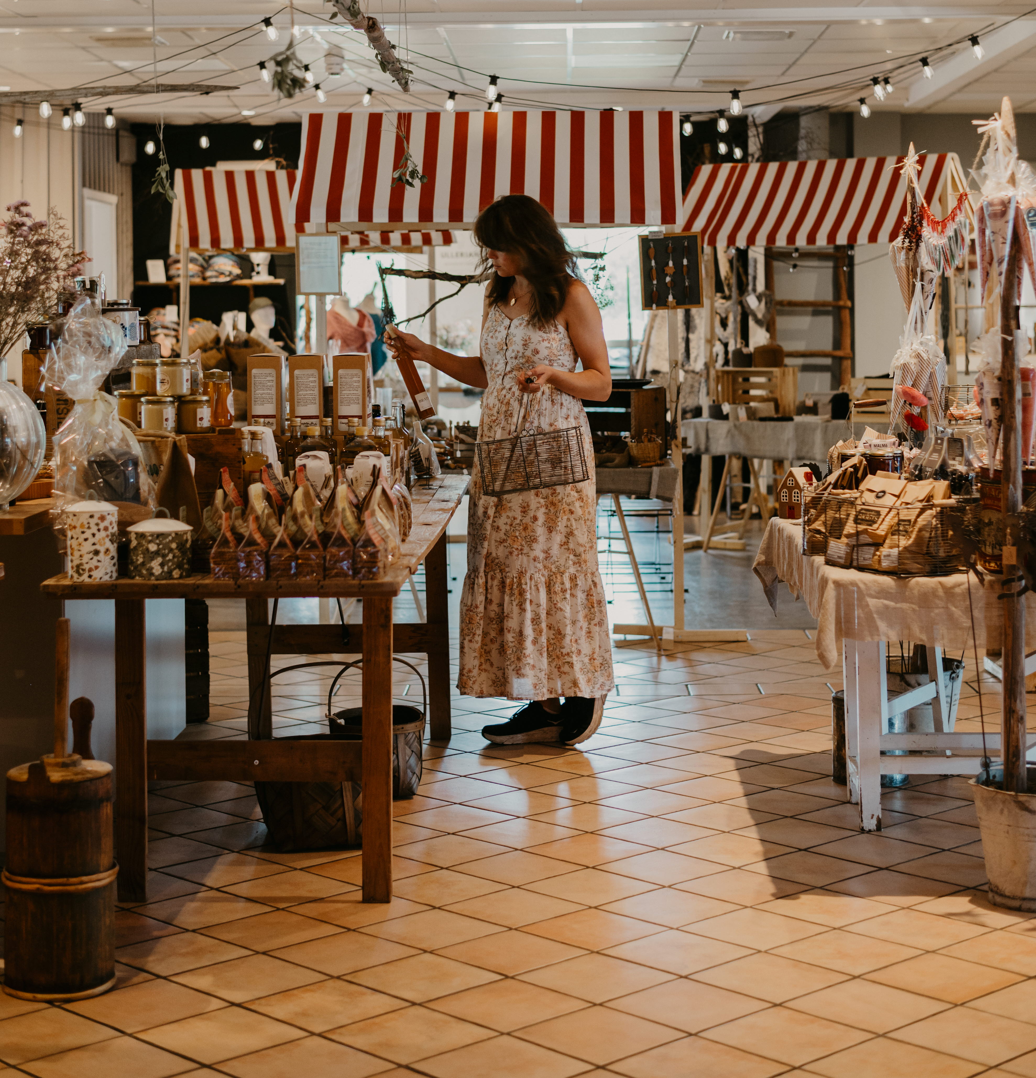 A woman walks around with a basket and looks at things in a shop.
