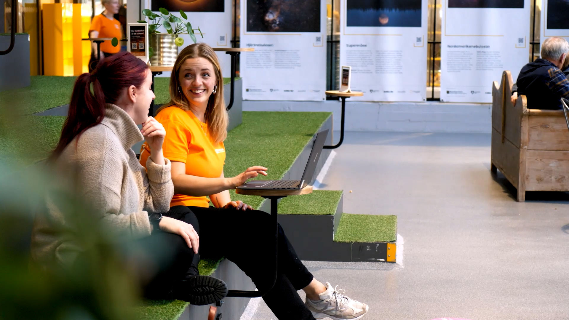 Två kvinnor sitter och pratar med varandra på ett science center.