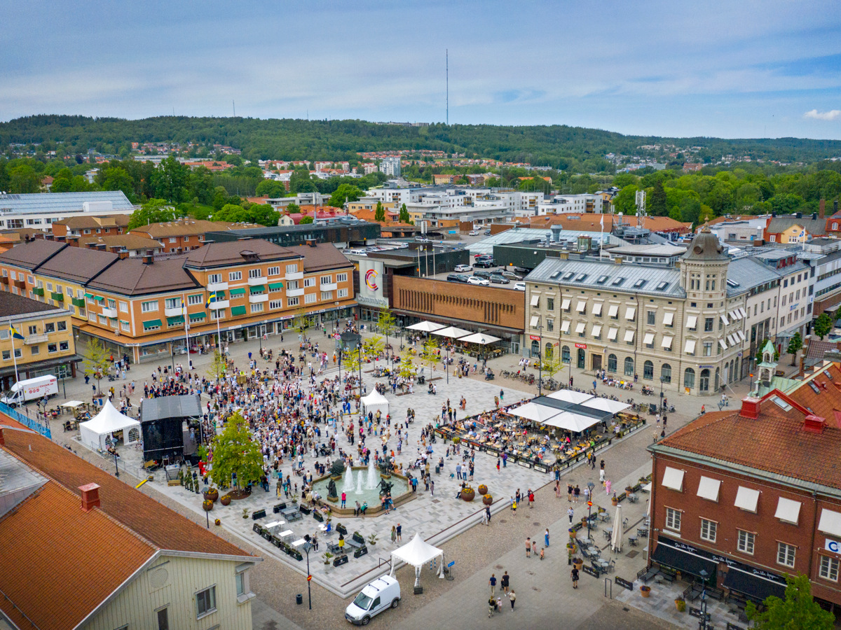 En flygbild på Hertig Johans torg i Skövde med många människor i rörelse. Runt torget syns byggnader.